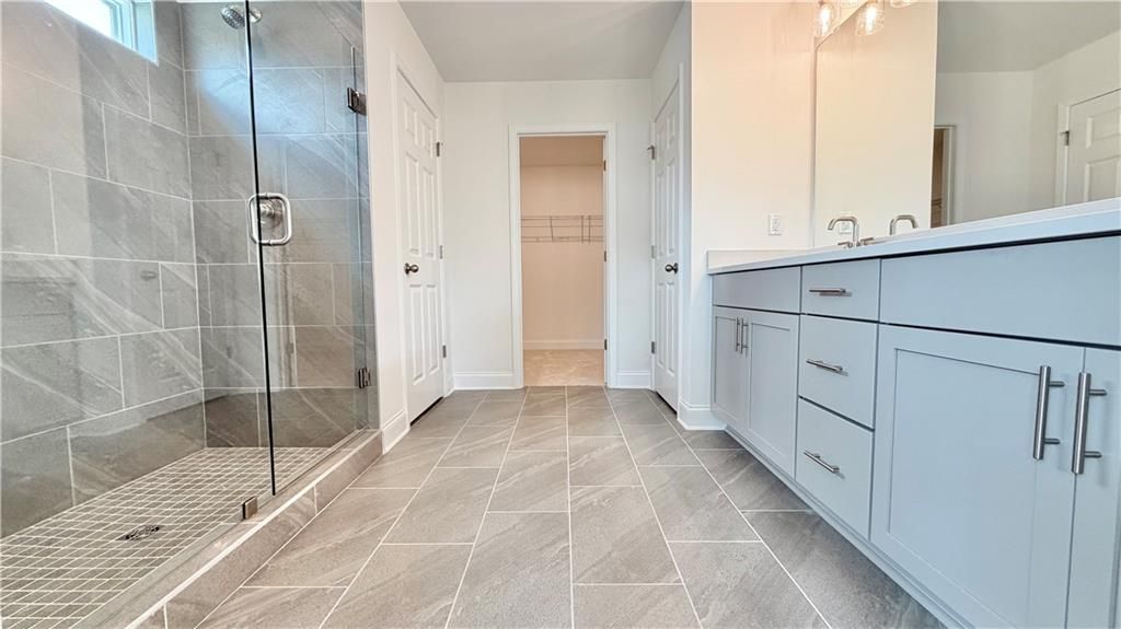 Modern primary bathroom with glass-enclosed tile shower and dual vanity in Davidson Homes The Hickory C, Hoschton, GA.