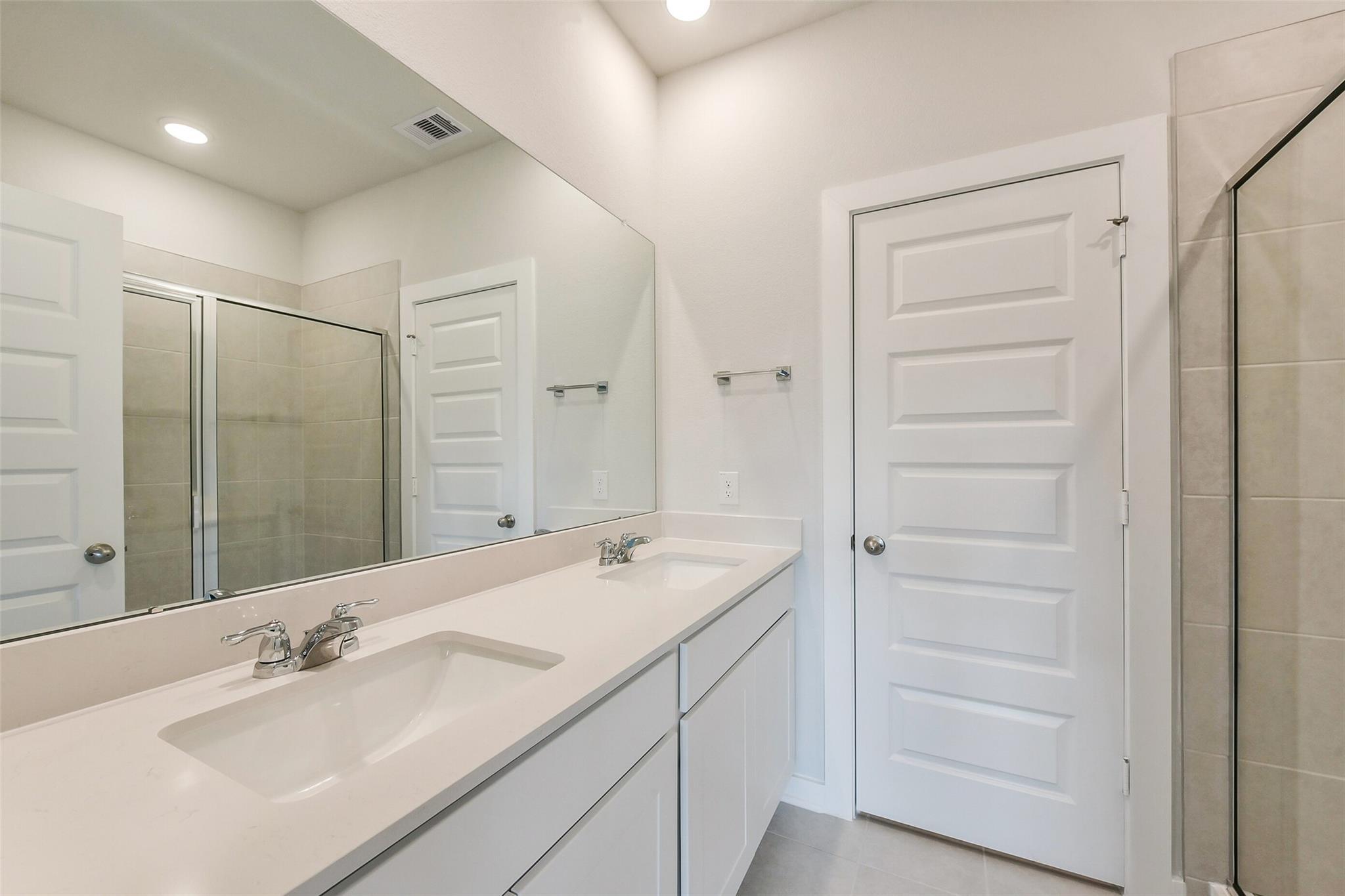 Modern master bathroom featuring double vanity sinks, large mirror, and glass walk-in shower in Davidson Homes The Frio G, Dayton, Texas