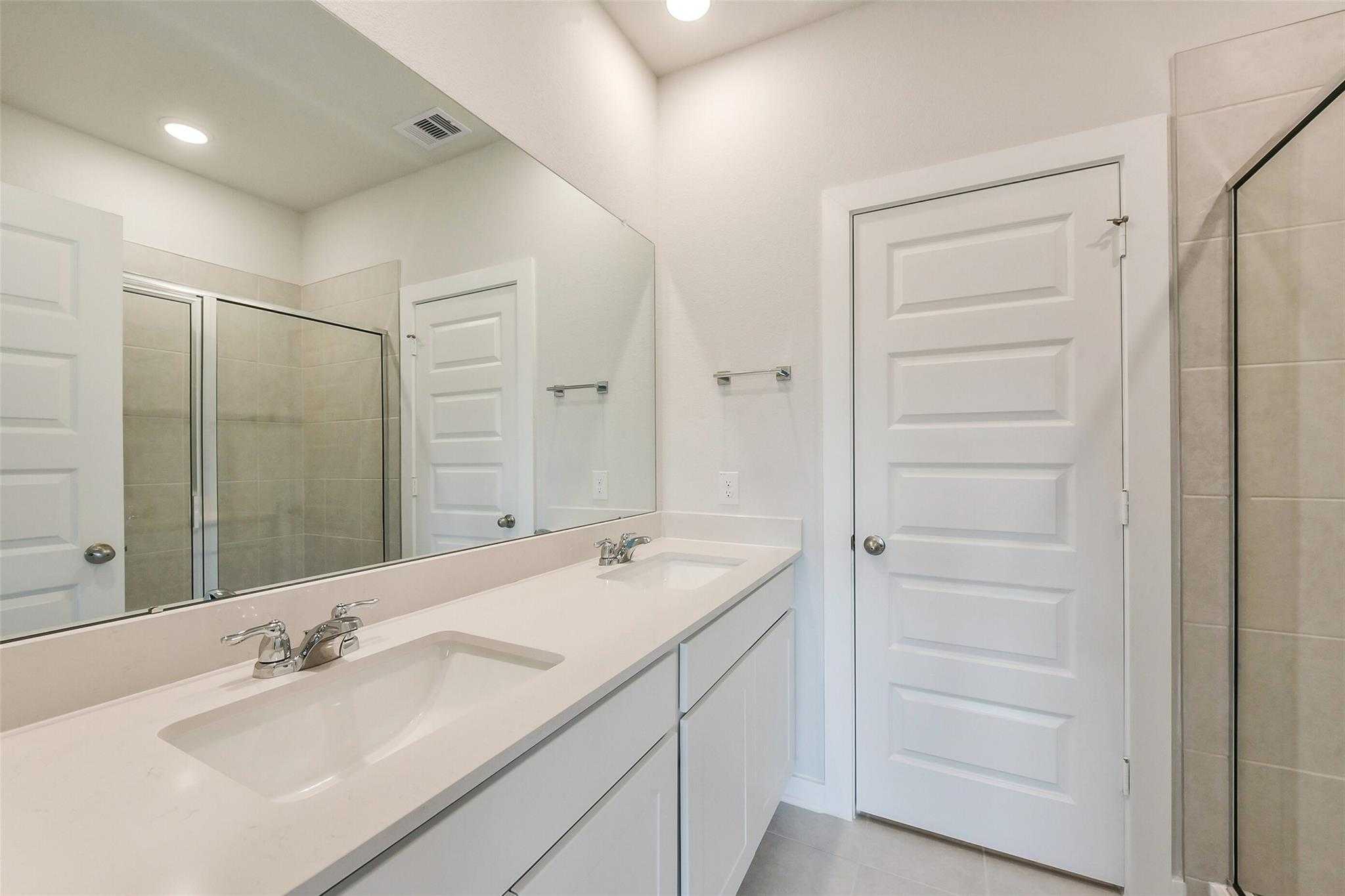 Modern master bathroom featuring double vanity sinks, large framed mirror, and glass shower door in Davidson Homes The Frio G, Dayton, Texas