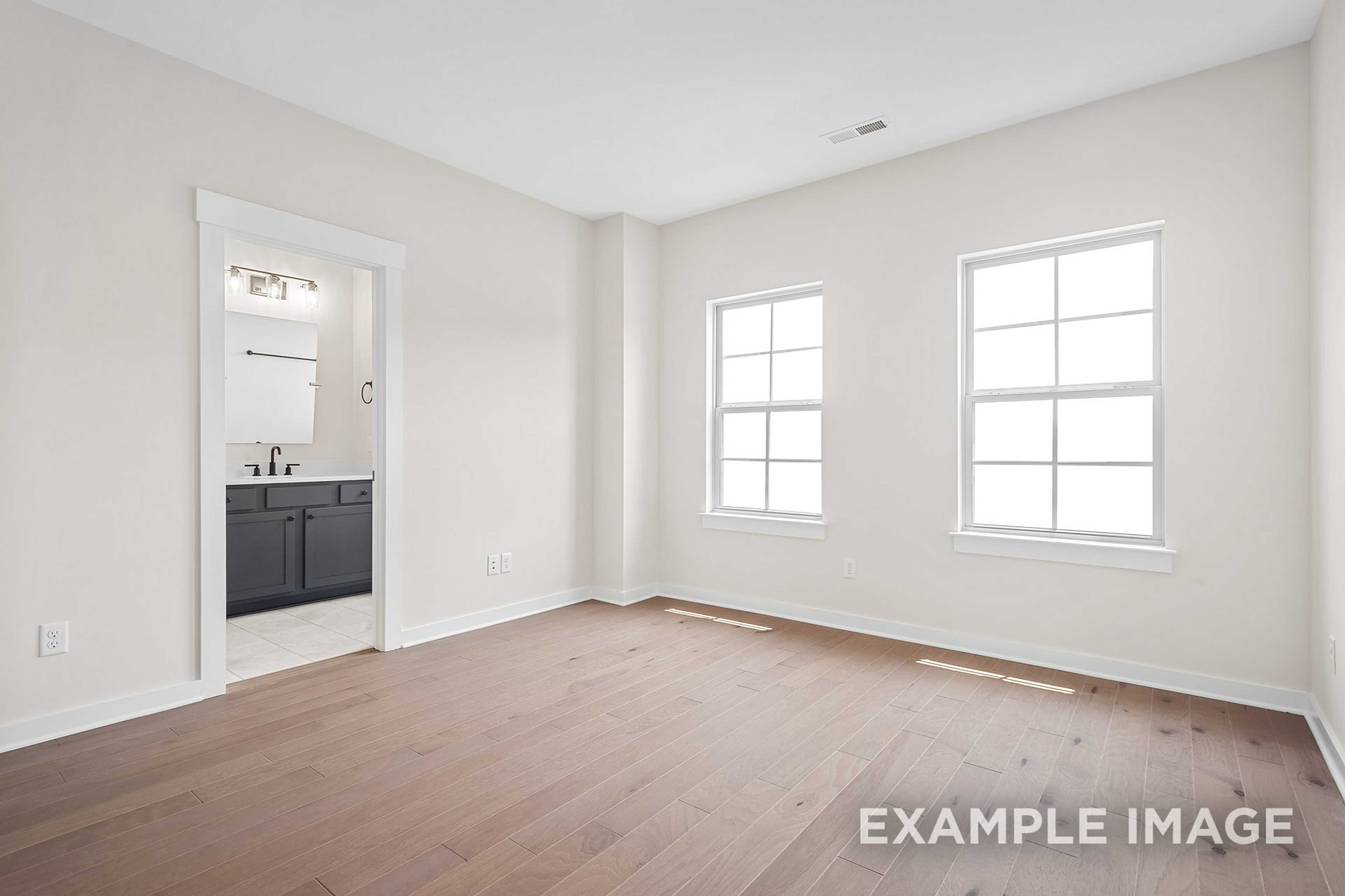 Spacious master bathroom in The Hawkins with beige walls, hardwood floors, double windows, and modern vanity sink