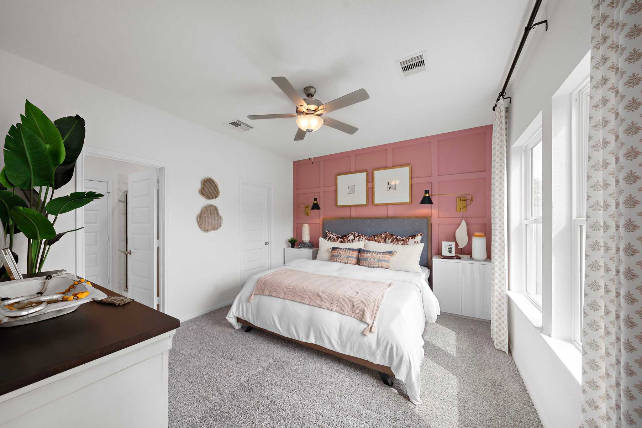 Primary bedroom with pink accent wall, upholstered king bed, and ceiling fan at The Villages at WestPointe in Dayton Texas