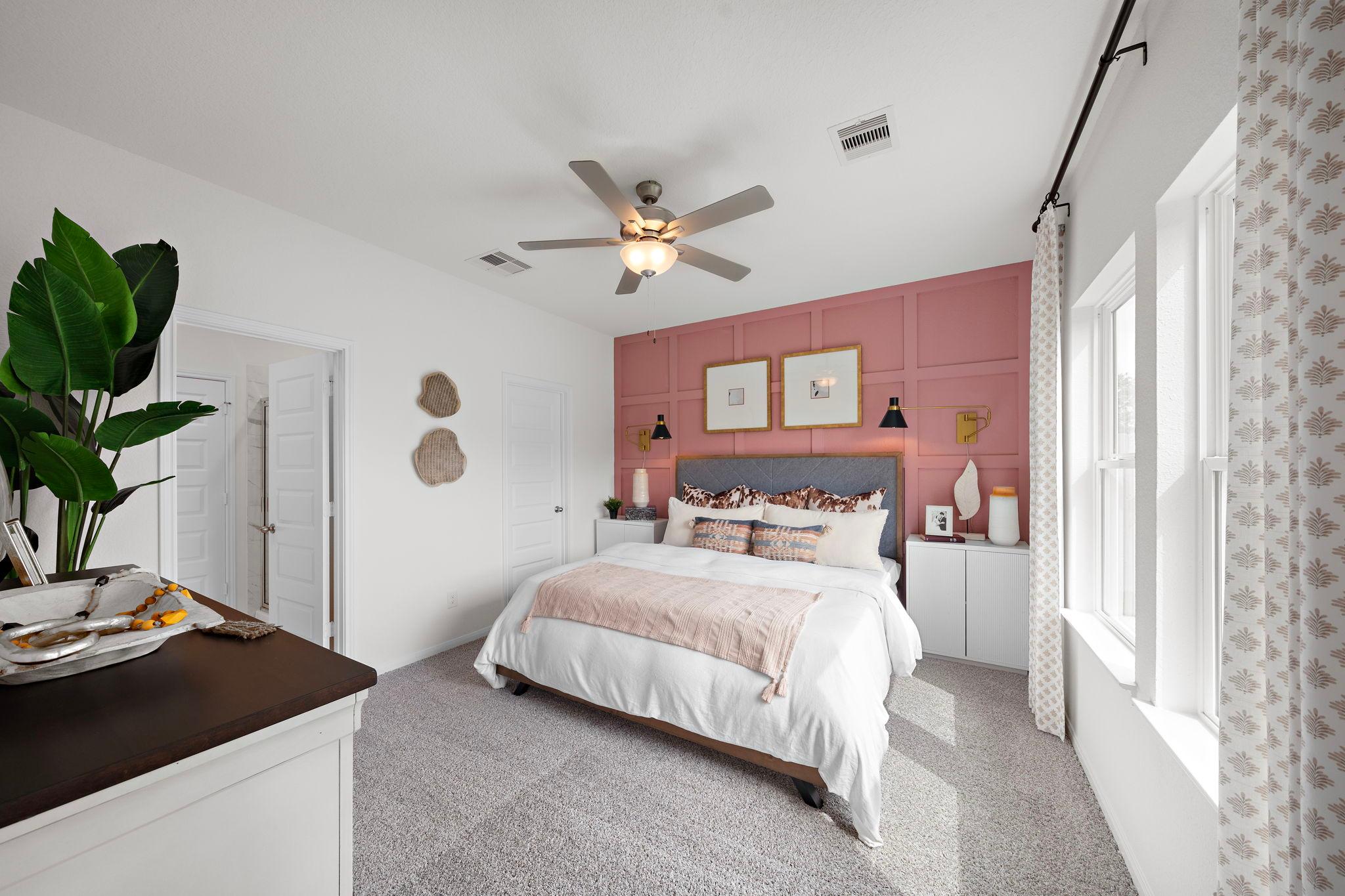 Primary bedroom with pink accent wall, upholstered king bed, and ceiling fan at The Villages at WestPointe in Dayton Texas