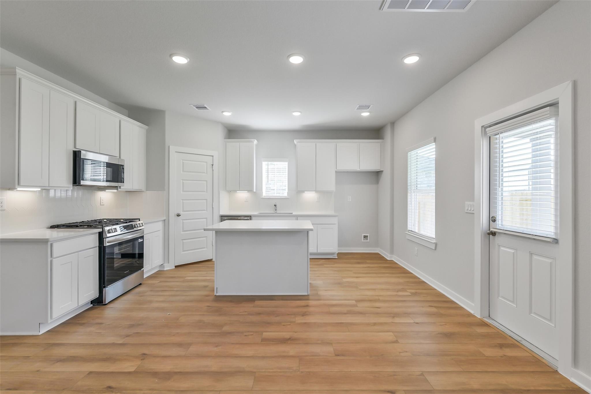 Modern white kitchen with stainless appliances, center island, and hardwood floors in Davidson Homes The Trinity F, Magnolia, TX