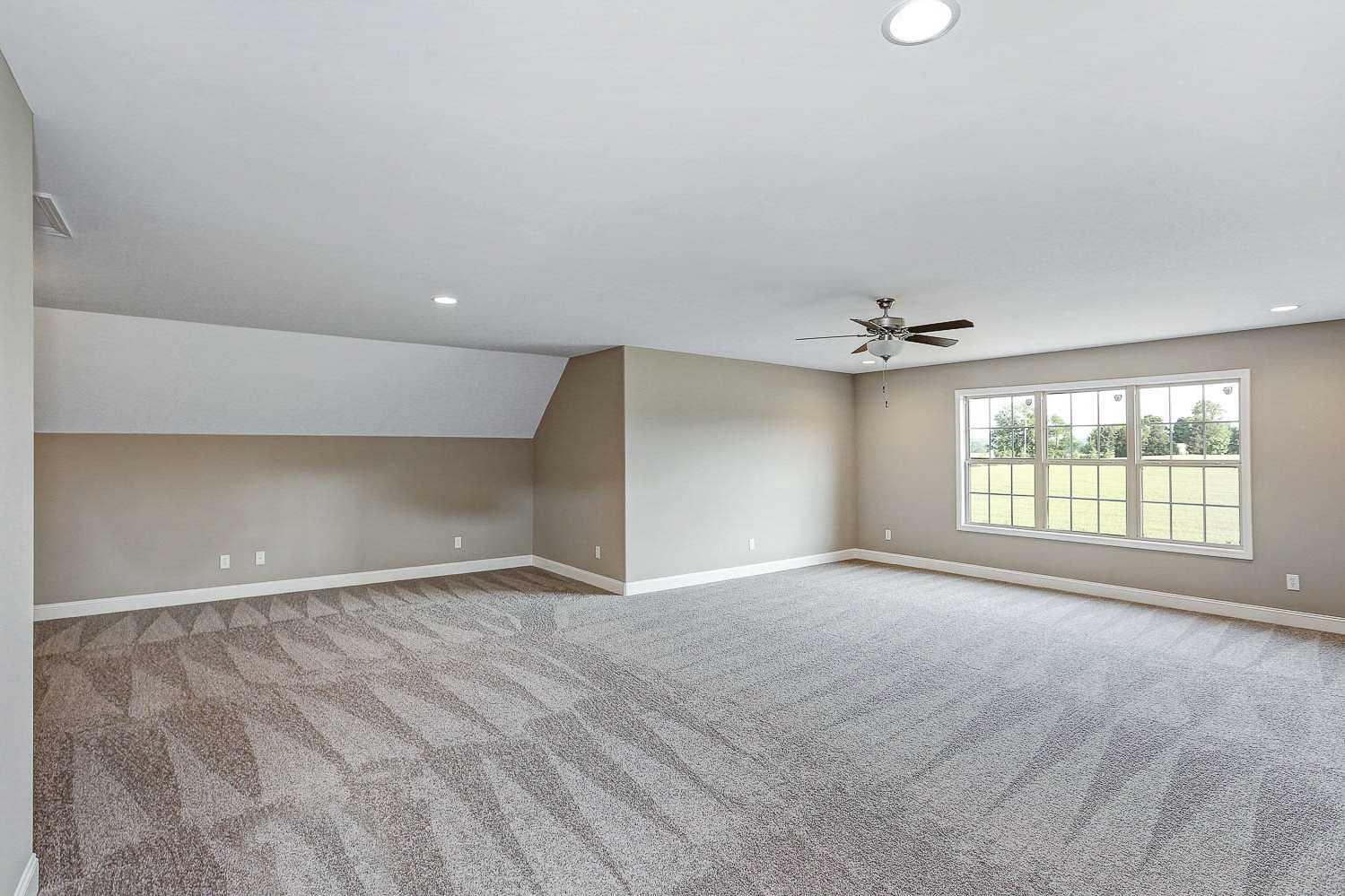 Spacious bonus room in The Montgomery home design with sloped ceiling, ceiling fan, and large windows overlooking green fields