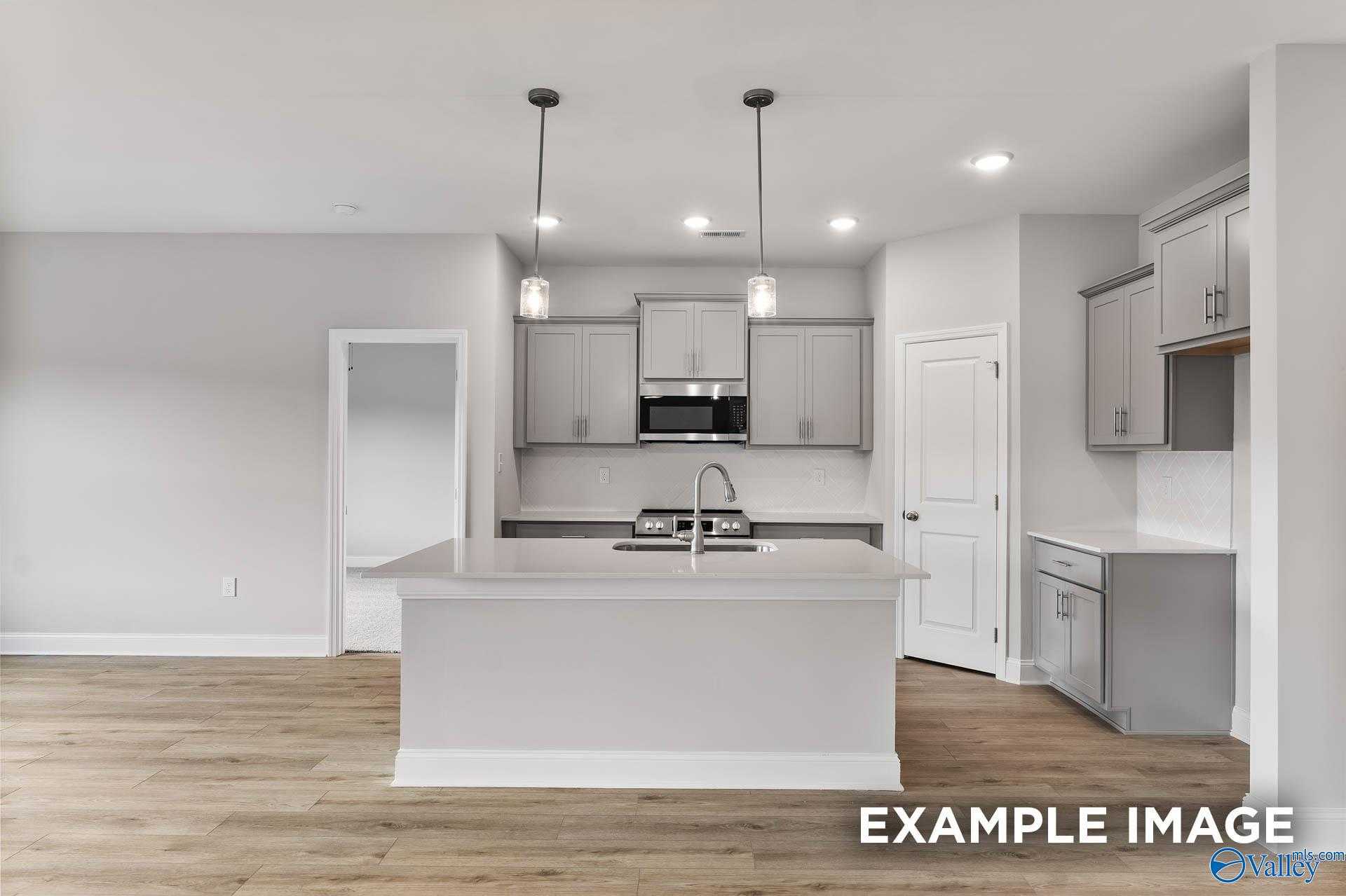 Modern white kitchen with large island, stainless appliances, and pendant lights in Davidson Homes The Franklin C, Toney, Alabama