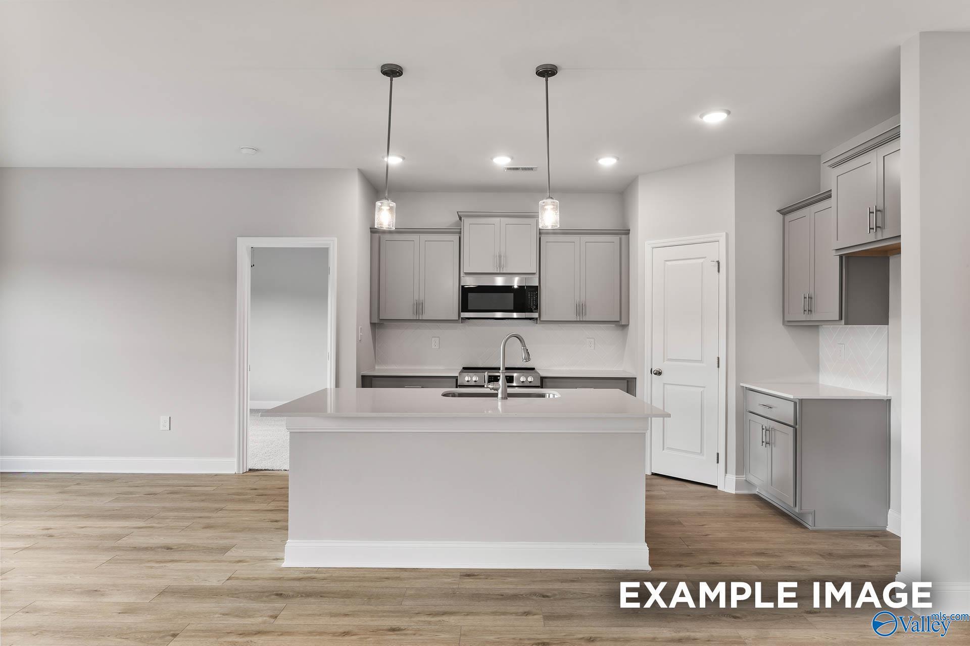 Modern white kitchen with quartz island, stainless appliances, pendant lights in Davidson Homes The Franklin, Athens, Alabama