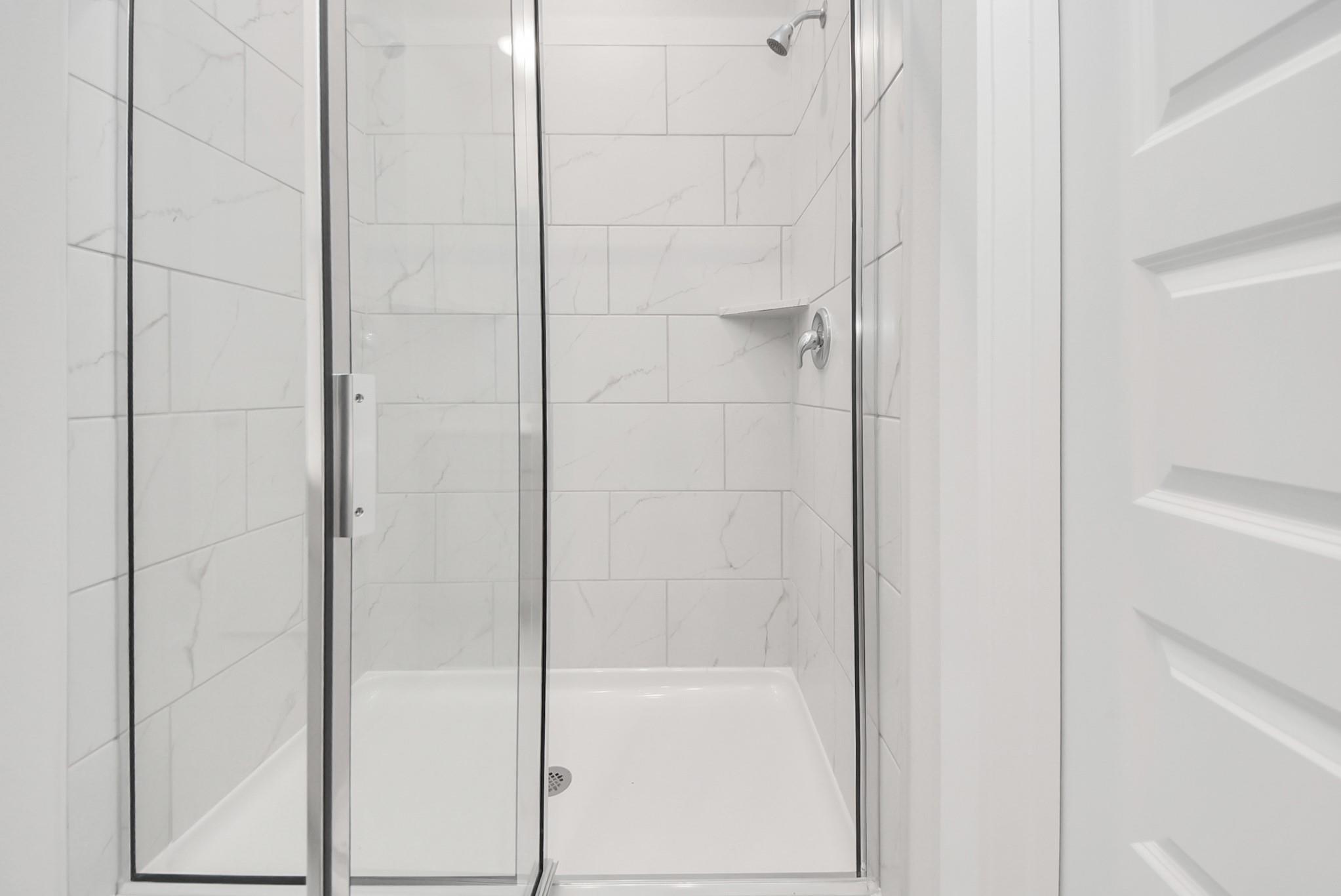 Modern walk-in shower with white marble-look subway tile in The Blanco F floor plan at Spring Branch Crossing, Conroe.
