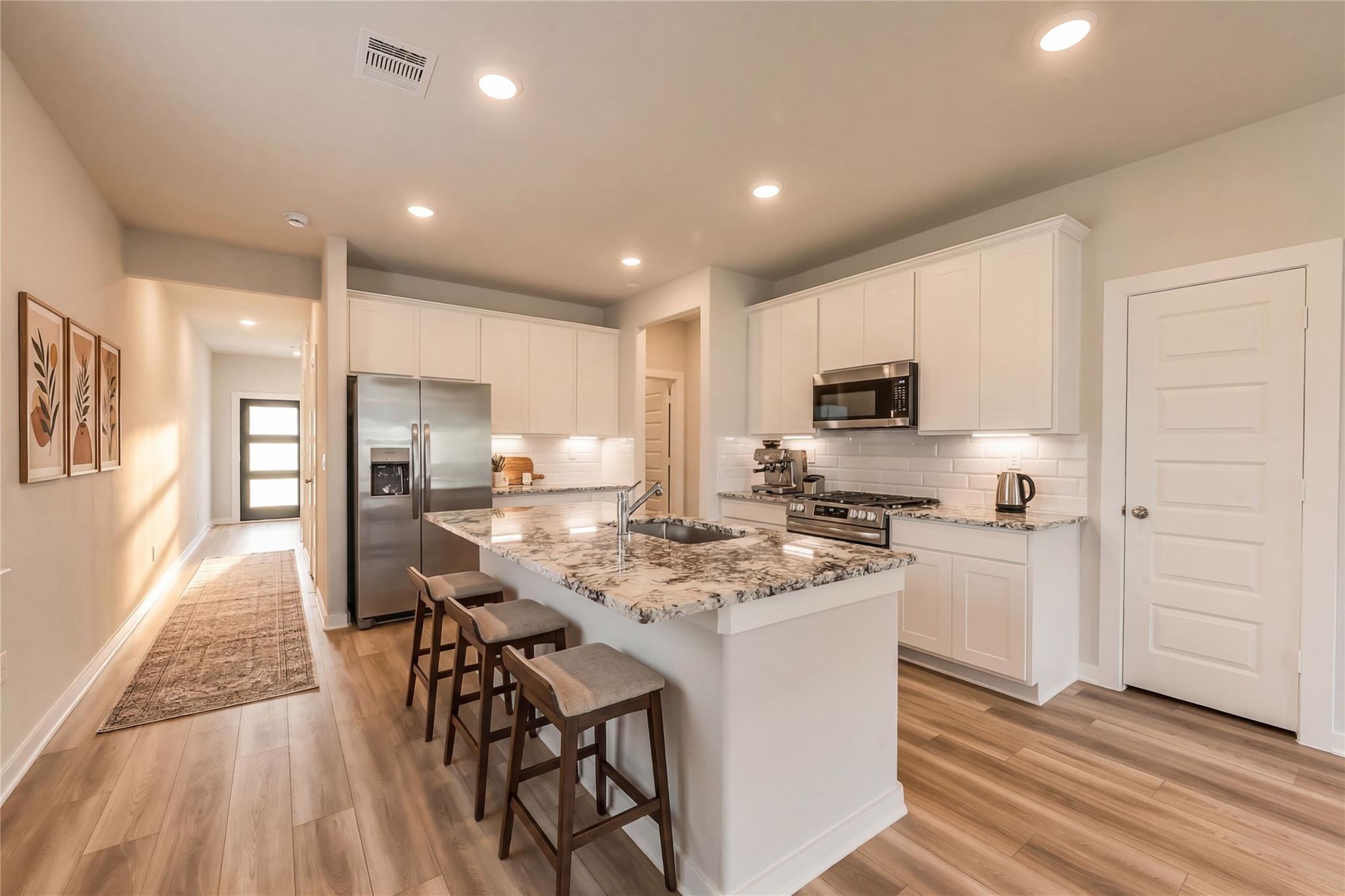 Modern white kitchen with granite island, stainless appliances, bar stools in The Frio G floor plan, Magnolia, Texas