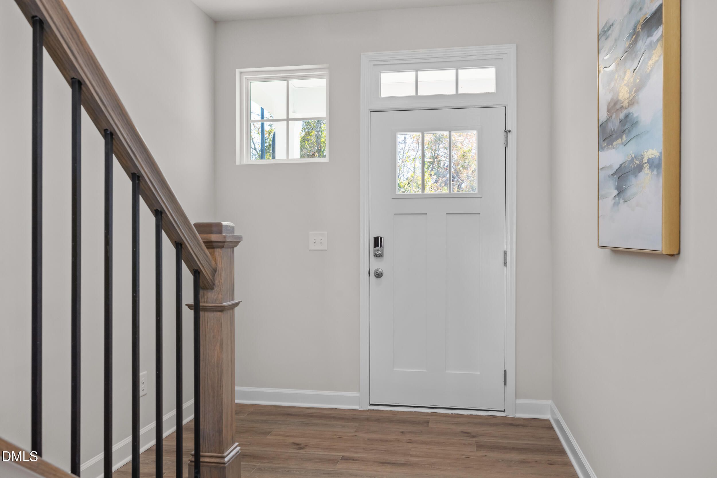 Bright foyer with wooden staircase, black railings, white entry door, and abstract wall art in Davidson Homes The Preston C, Lillington, NC