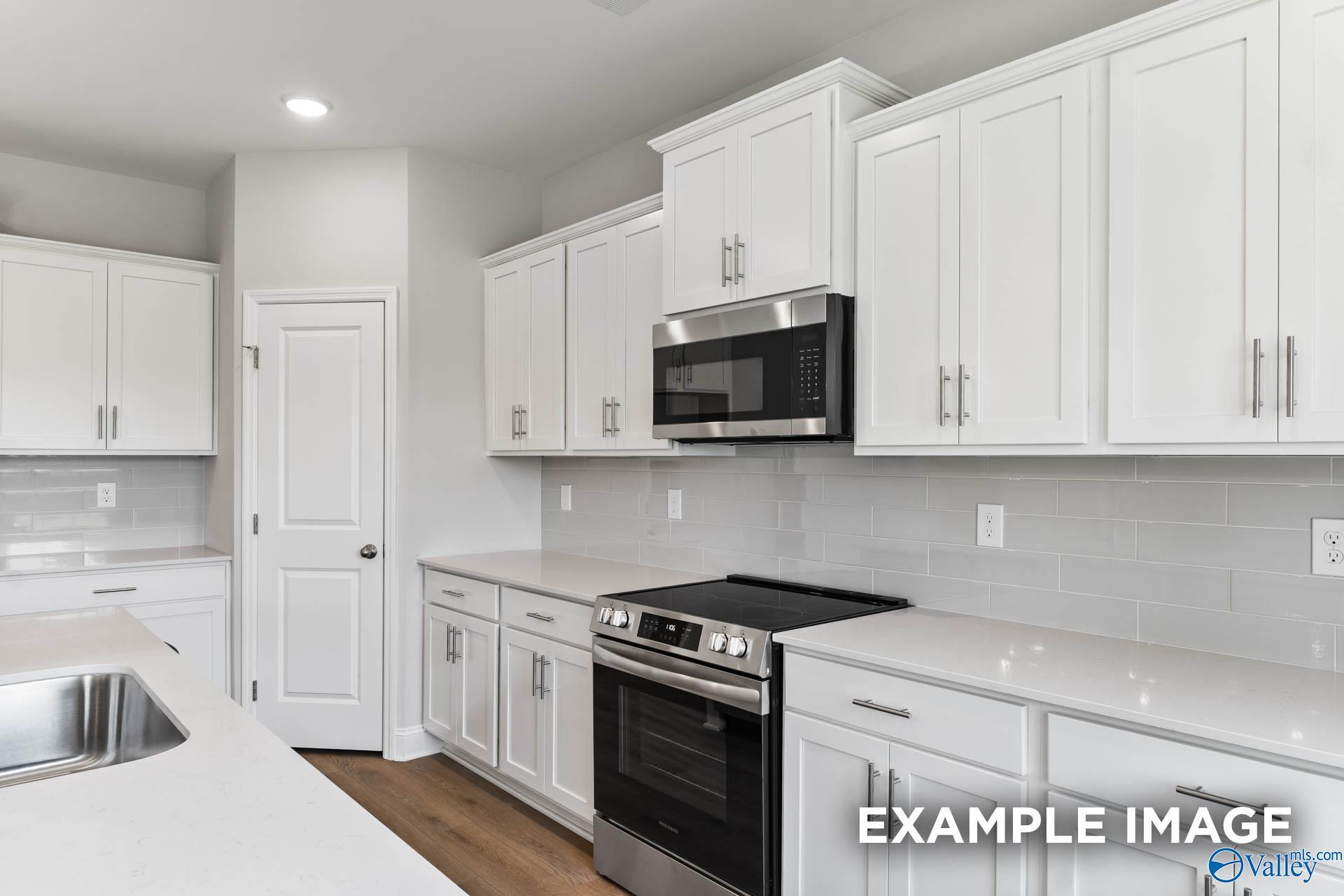 Modern kitchen with white cabinets, quartz countertops, and stainless appliances in The Madison A plan, The Meadows, Athens.
