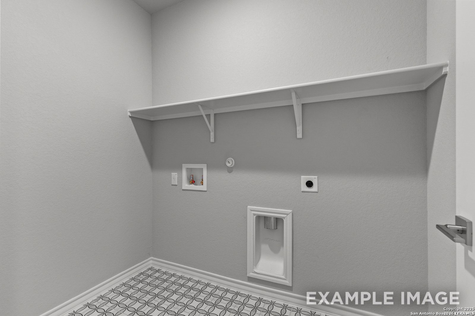 Laundry room with patterned tile floor, storage shelf, and utility hookups in Davidson Homes Oxford F plan in Castroville.