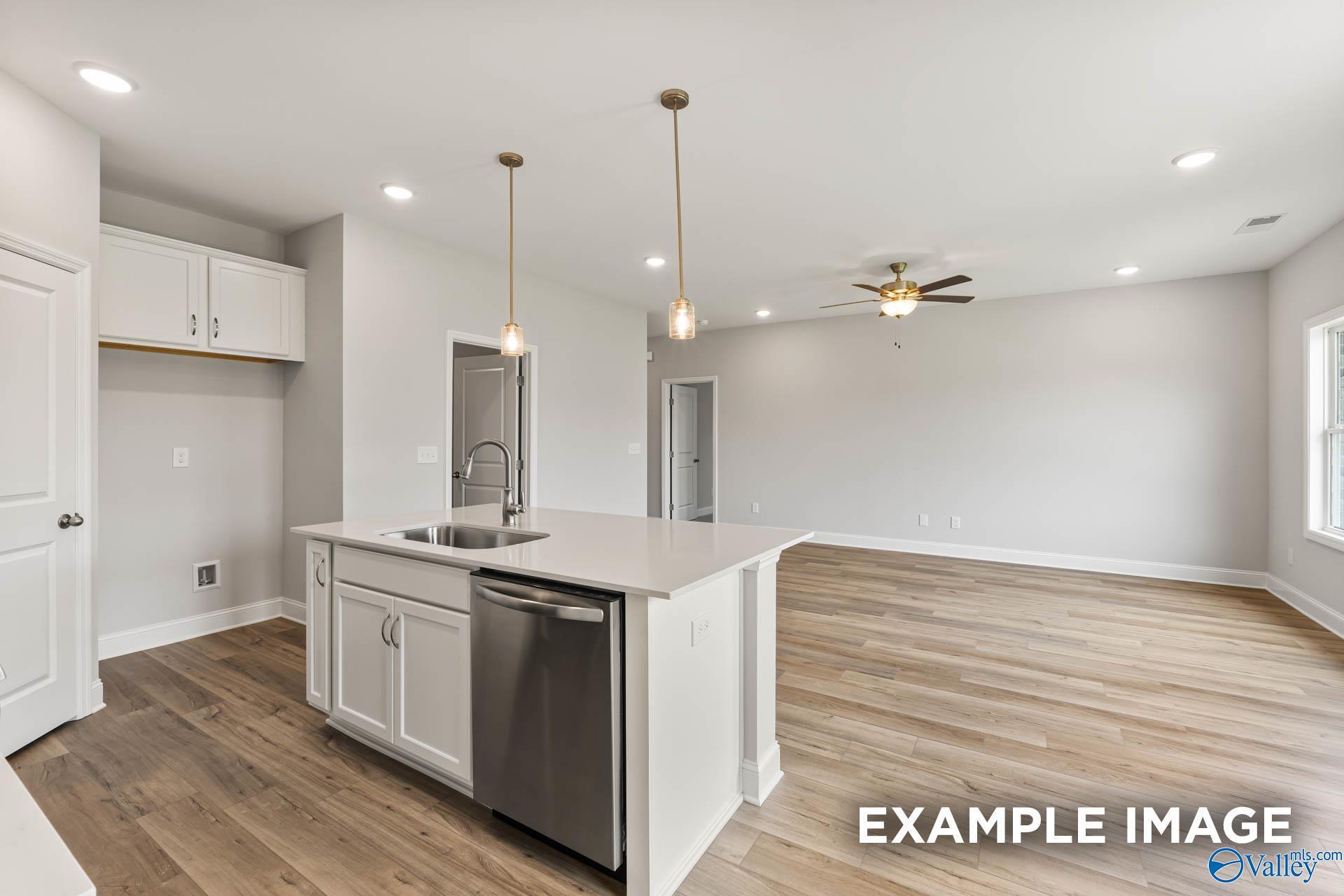 White kitchen island with sink and pendant lights beside open living area in Davidson Homes The Butler floor plan, Arab, Alabama