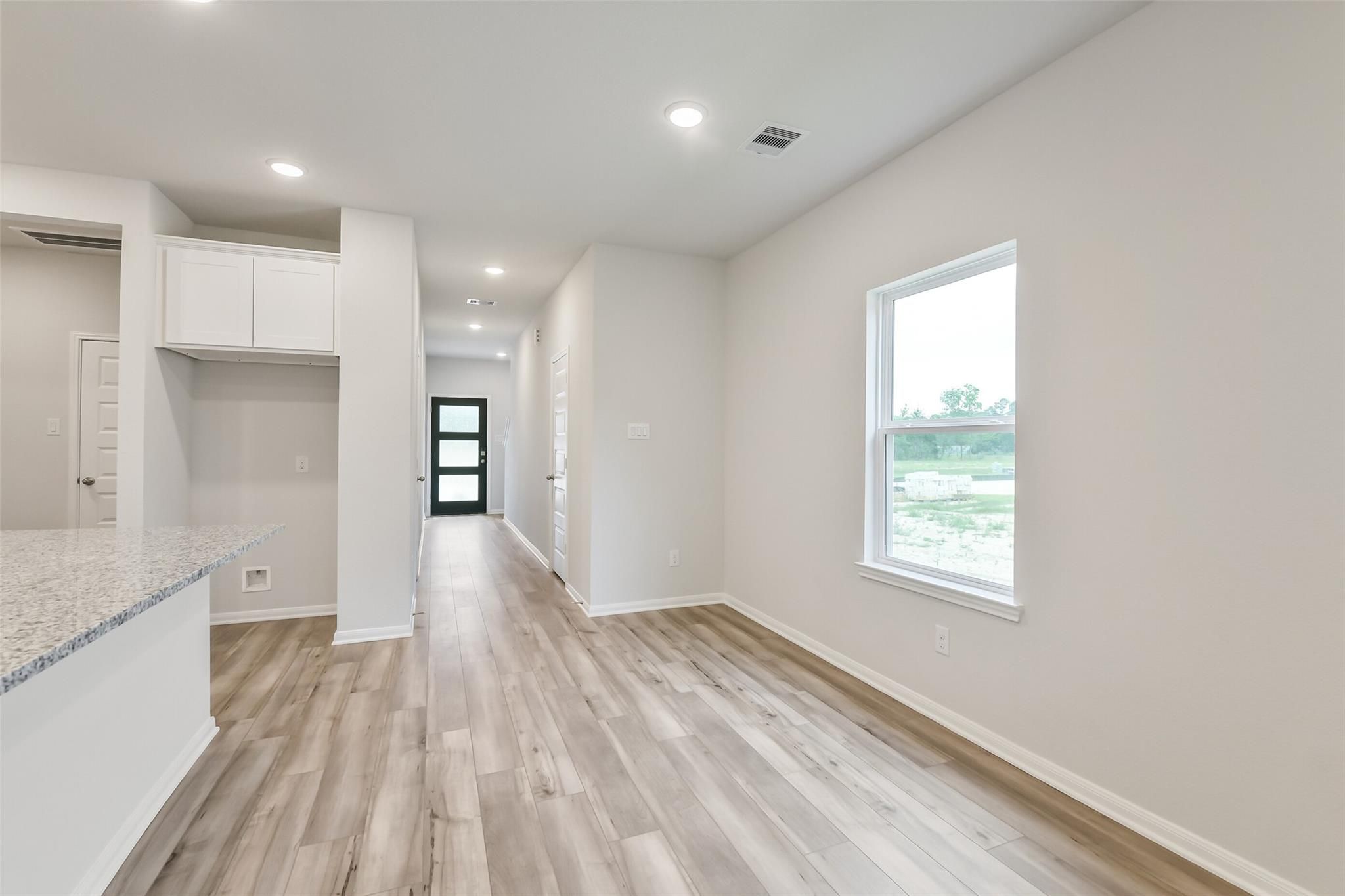 Bright kitchen with granite island, white cabinets, and hallway featuring luxury wood-look flooring in The Brazos F, Conroe, Texas