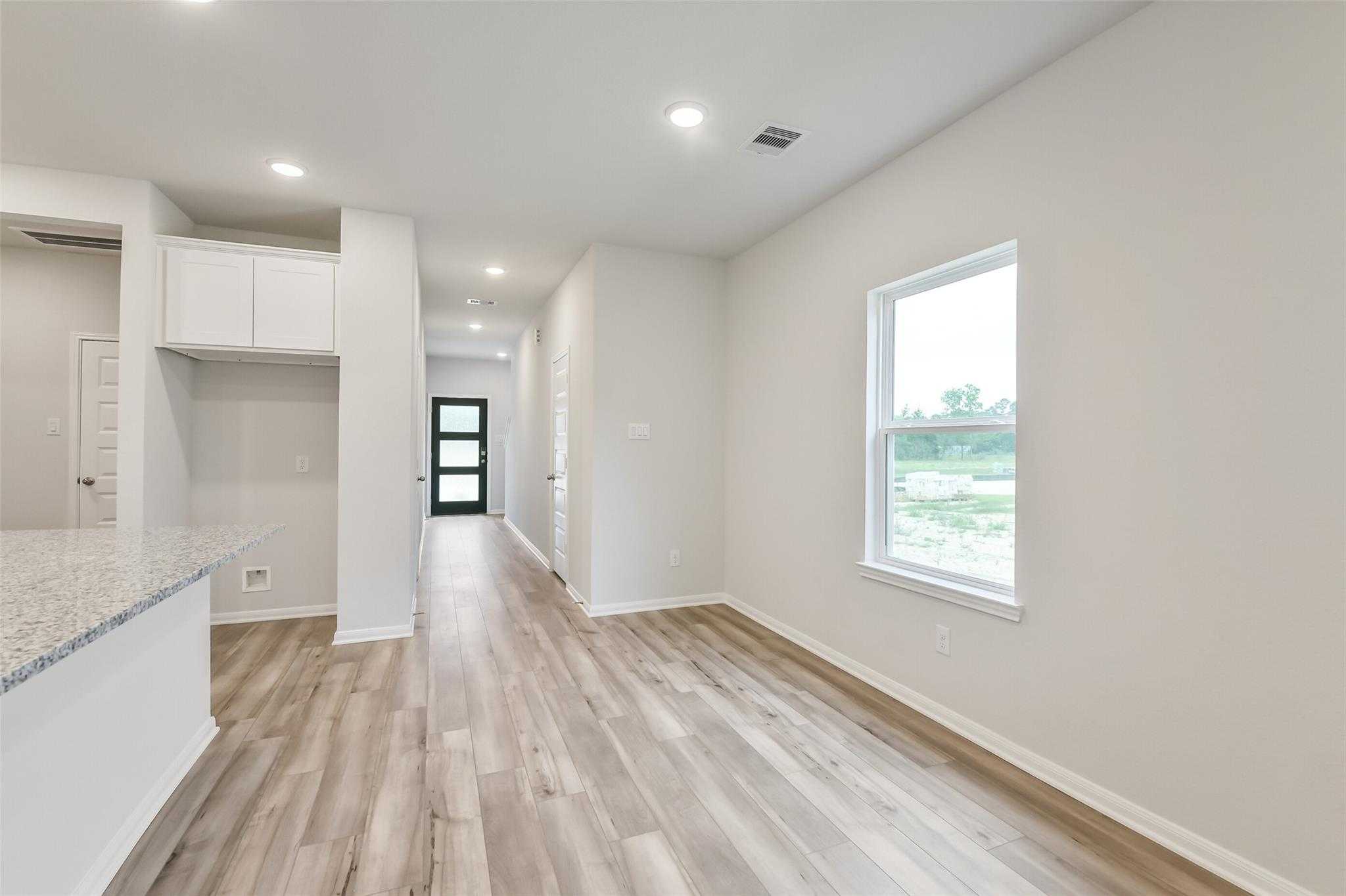 Bright kitchen with granite island, white cabinets, and hallway featuring luxury wood-look flooring in The Brazos F, Conroe, Texas
