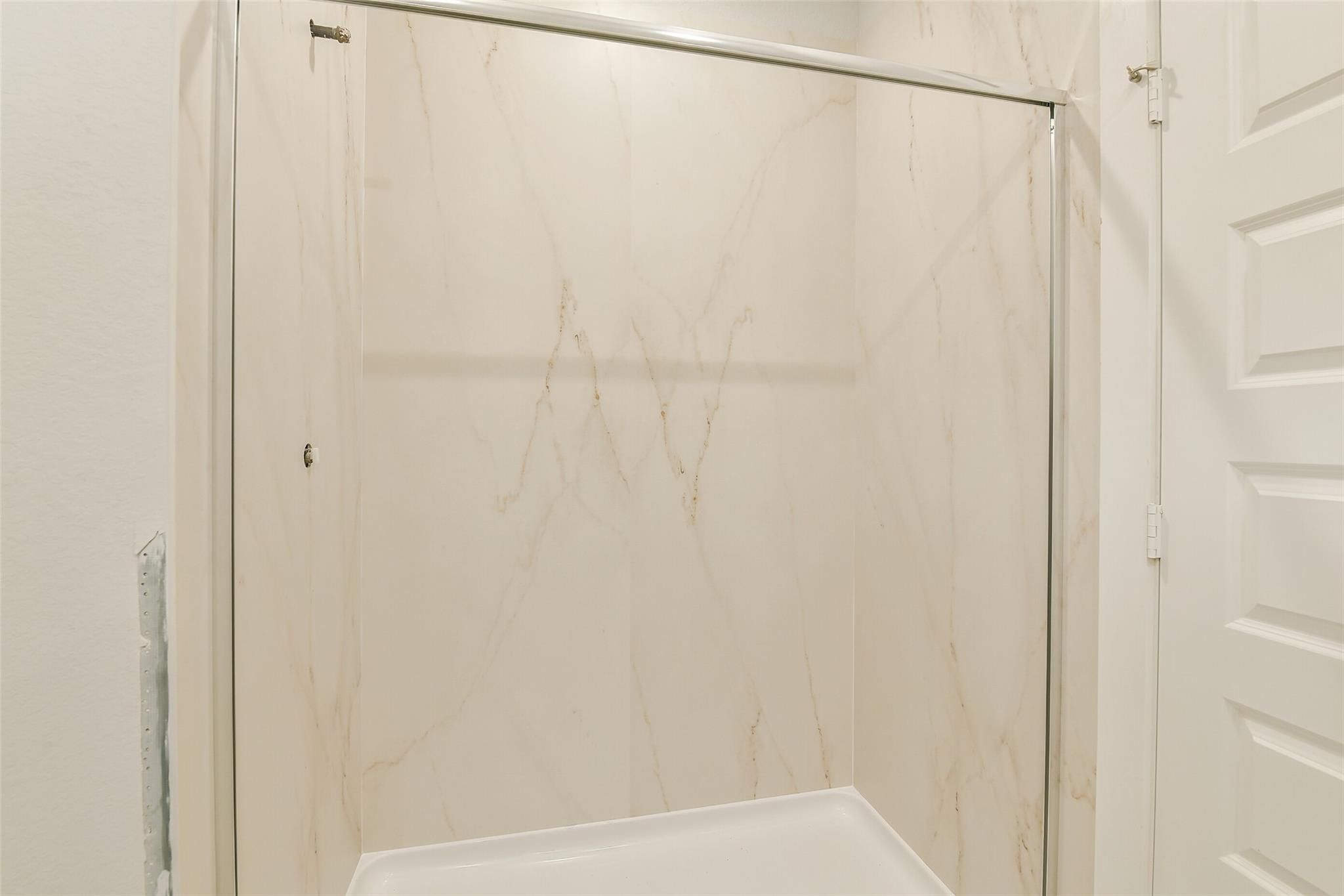 Elegant marble-look shower enclosure with glass door in Davidson Homes The Colorado F bathroom, Cleveland, Texas