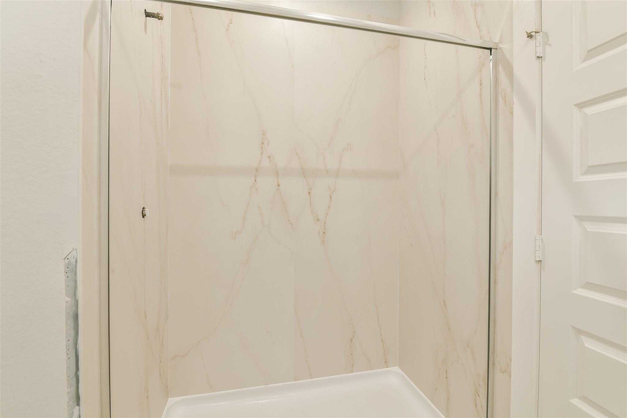 Modern shower with sliding glass door and marble-patterned tile walls in Davidson Homes The Colorado F bathroom, Cleveland, Texas