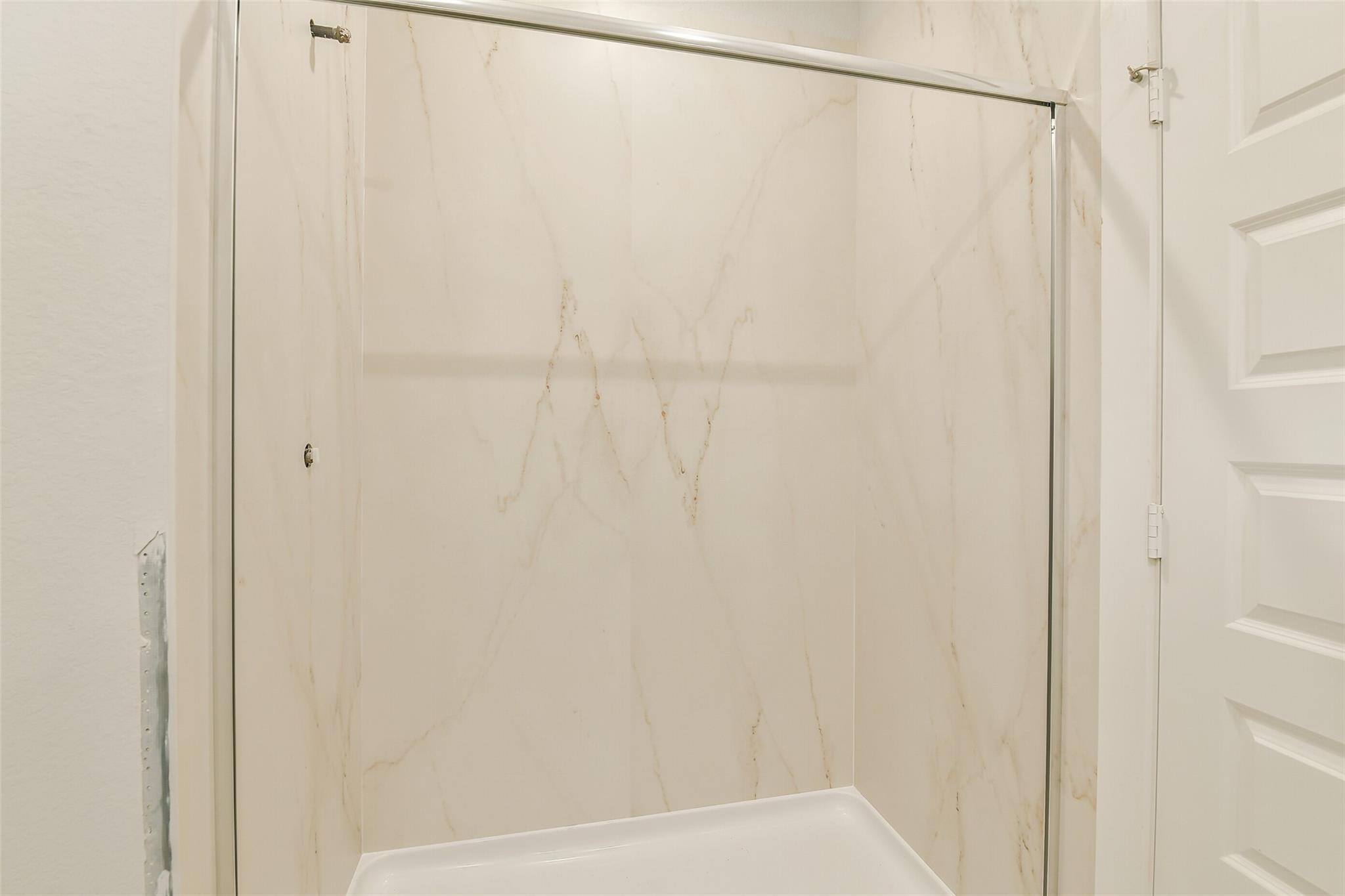 Modern glass shower enclosure with marble-patterned panels in master bath of Davidson Homes Colorado F, Cleveland, Texas