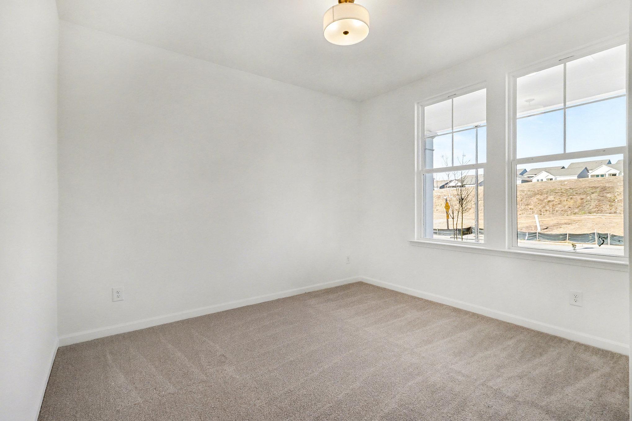 Bright bedroom with large windows overlooking wooded lot, white doors, beige walls, gray carpet in Davidson Homes The Daphne B, Loganville, GA
