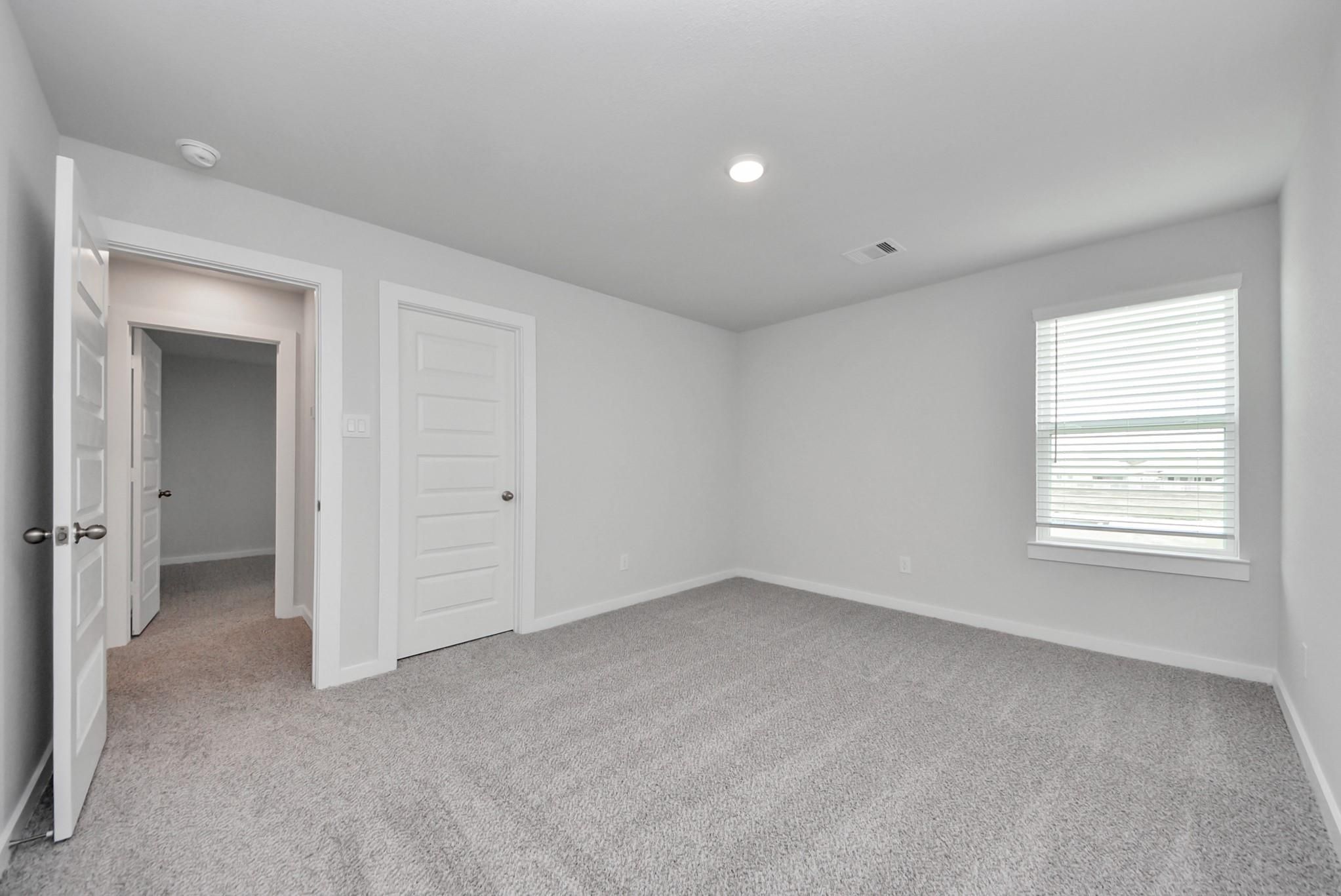 Spacious carpeted bedroom with white doors and window blinds in Davidson Homes San Marcos E floor plan, Emberly, Beasley, Texas