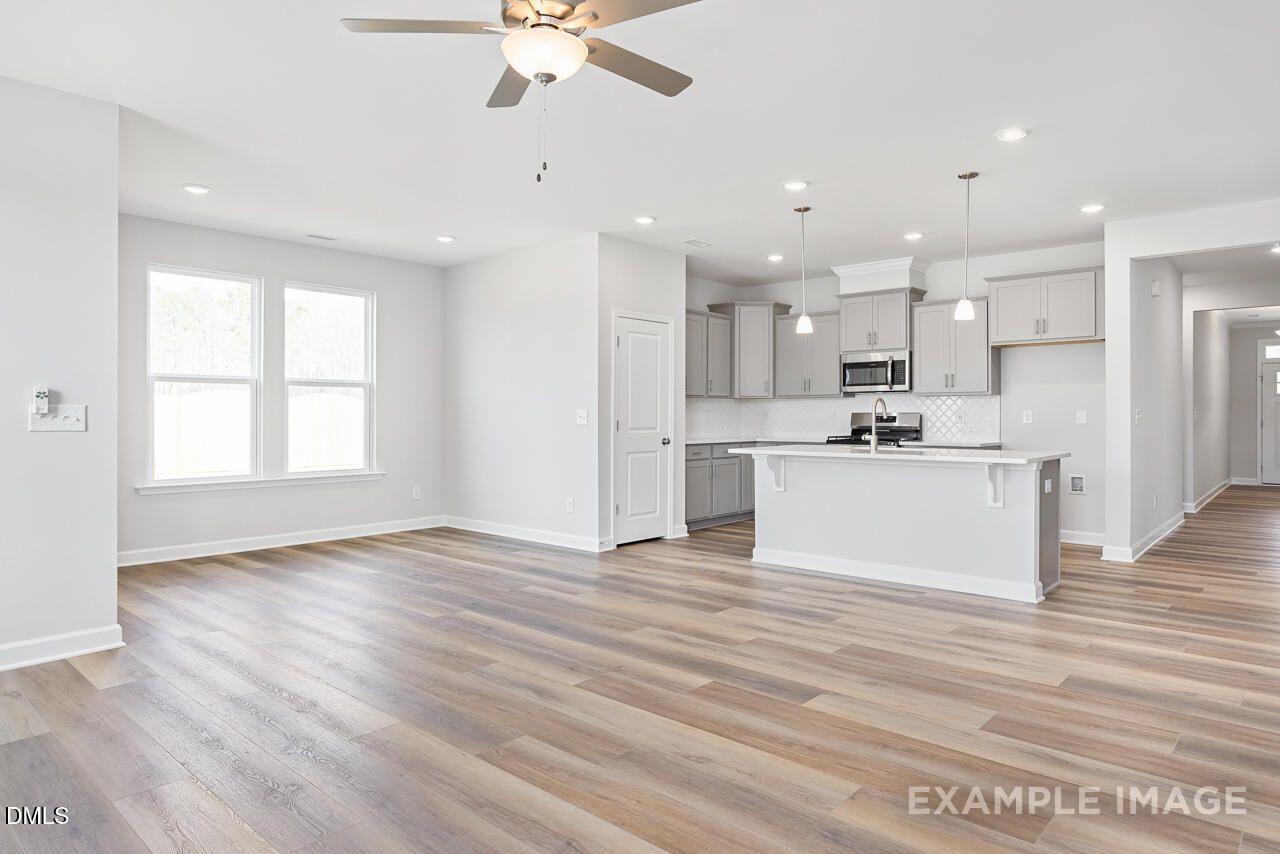 Bright open-concept kitchen-living area with white island, stainless microwave, ceiling fan, luxury vinyl plank floors in The Daphne C, Lillington NC