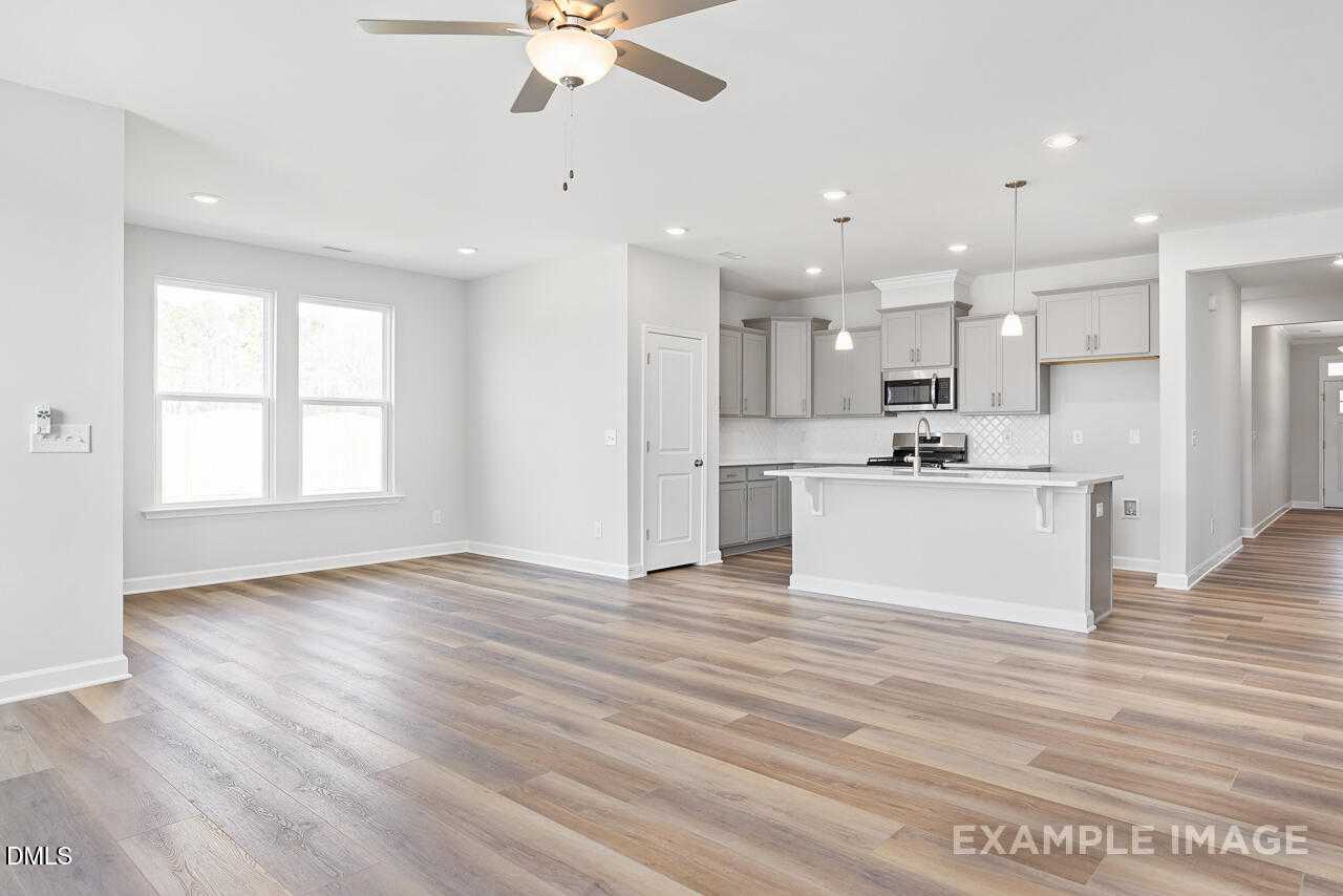 Bright open-concept kitchen-living area with white island, stainless microwave, ceiling fan, luxury vinyl plank floors in The Daphne C, Lillington NC