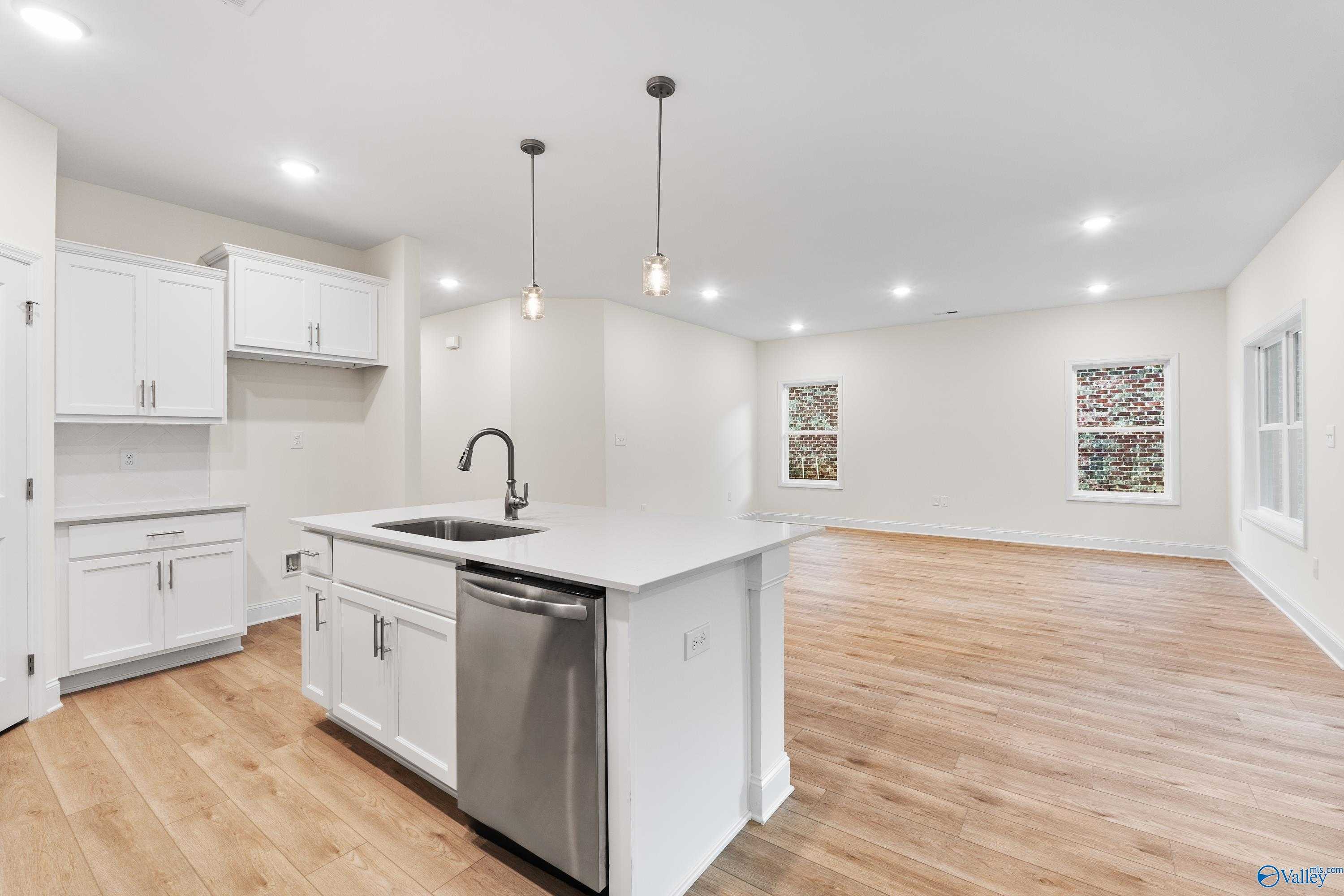 Modern open-concept kitchen with white island cabinets, stainless dishwasher, sink, hardwood floors in Davidson Homes The Franklin C, Huntsville AL