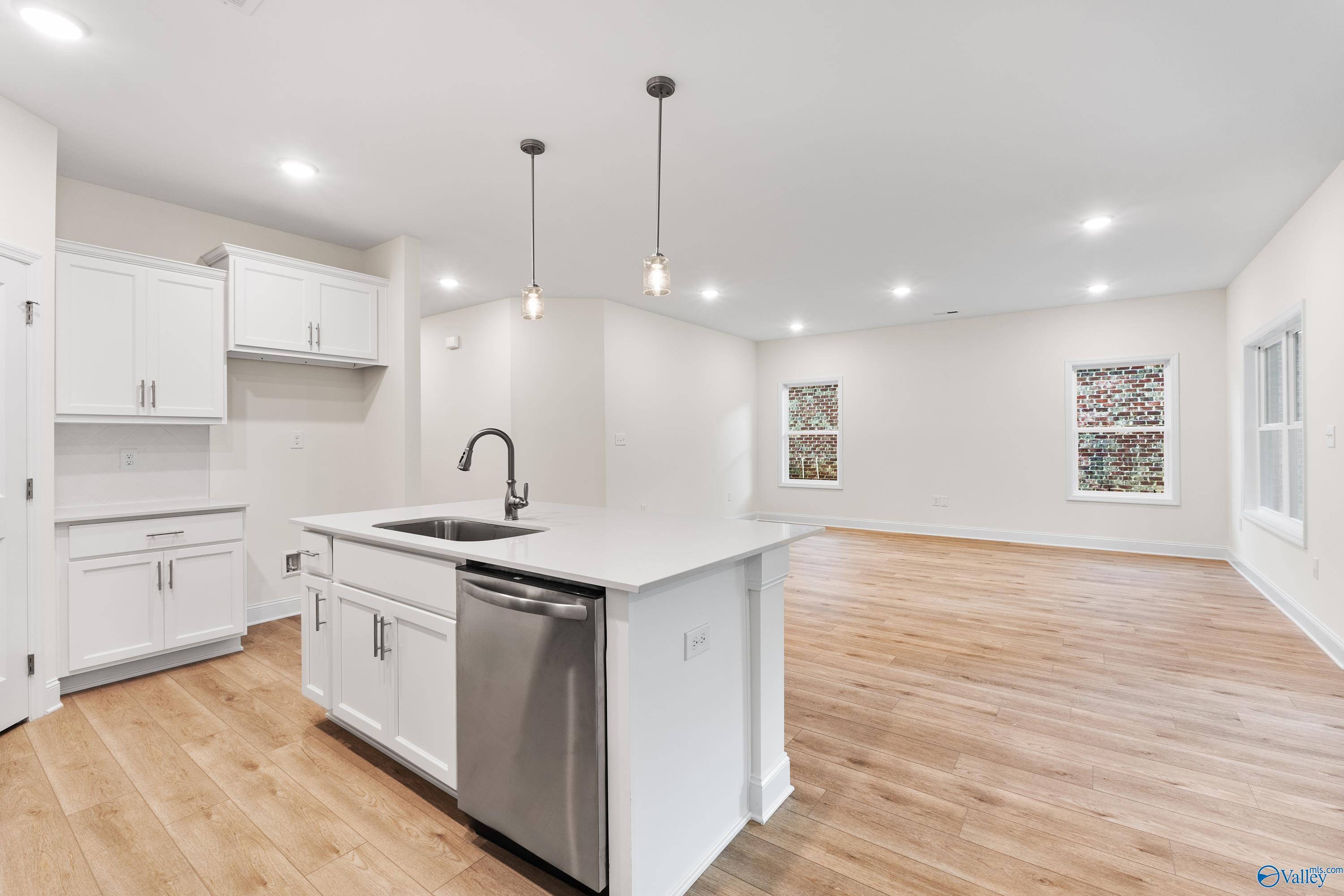 Modern open-concept kitchen with white island cabinets, stainless dishwasher, sink, hardwood floors in Davidson Homes The Franklin C, Huntsville AL