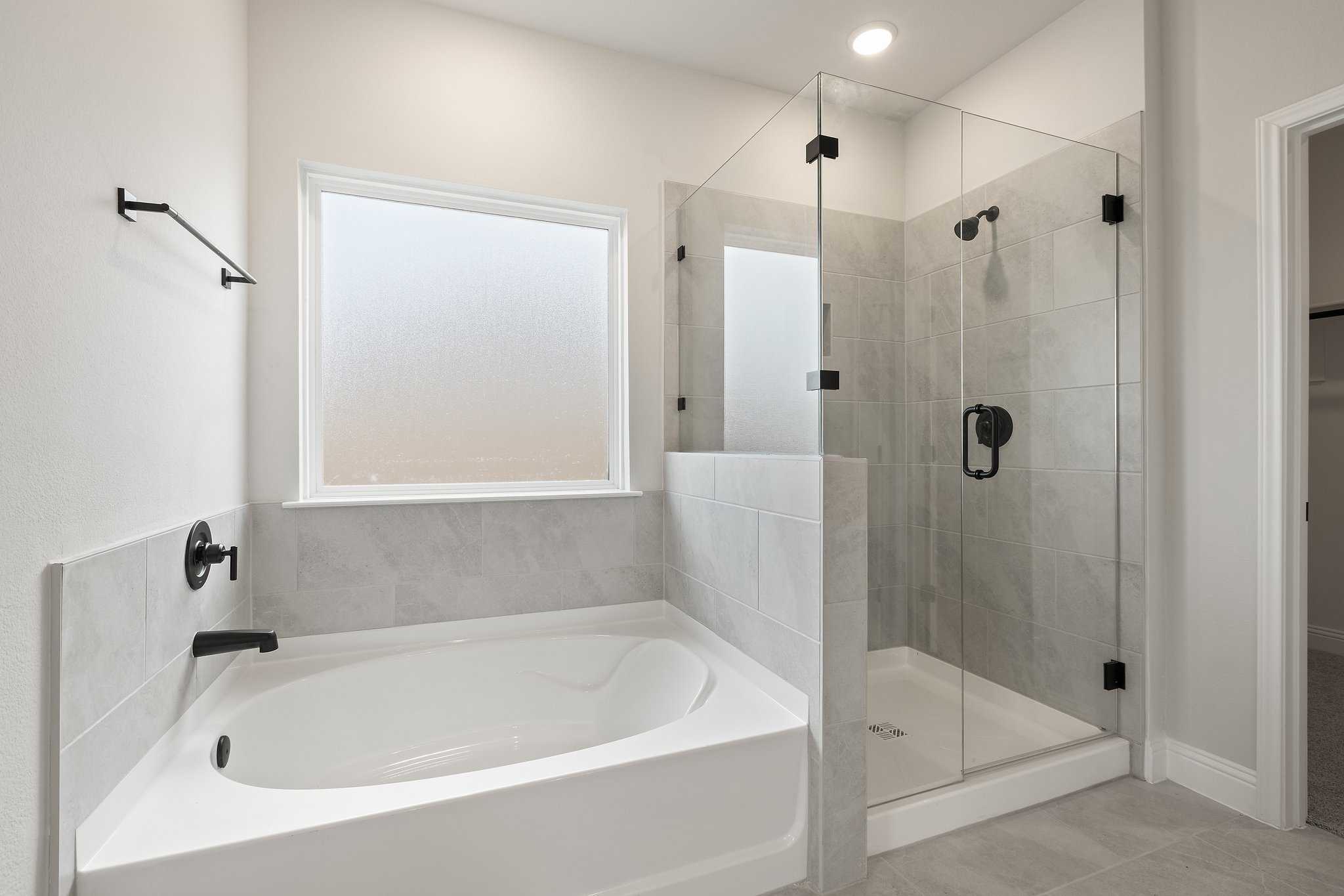 The Harrison C master bathroom with freestanding soaking tub, frameless glass shower, and gray tile accents