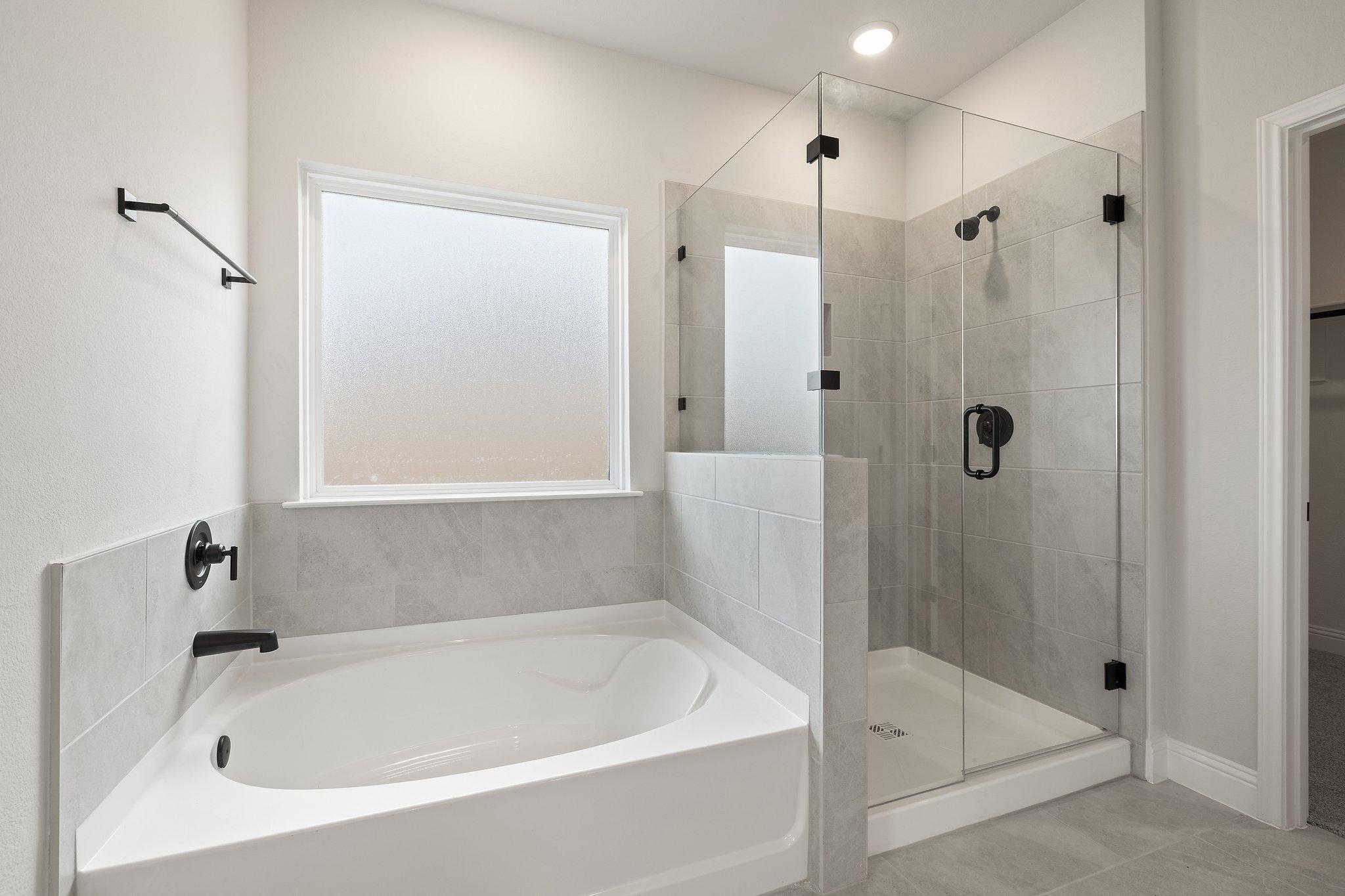 Luxurious master bathroom in The Harrison featuring freestanding tub, frameless glass shower, and frosted window