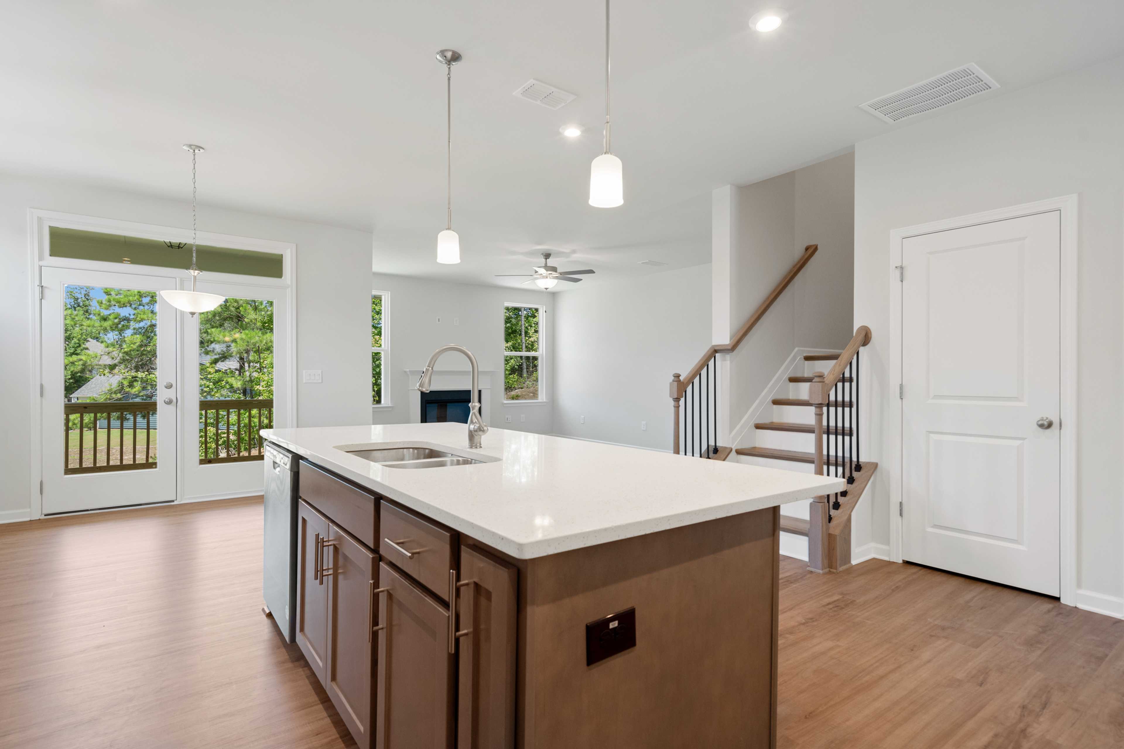 Open-concept kitchen living area in Mountainbrook Cartersville GA home with white quartz island, hardwood floors, French doors to deck, and fireplace