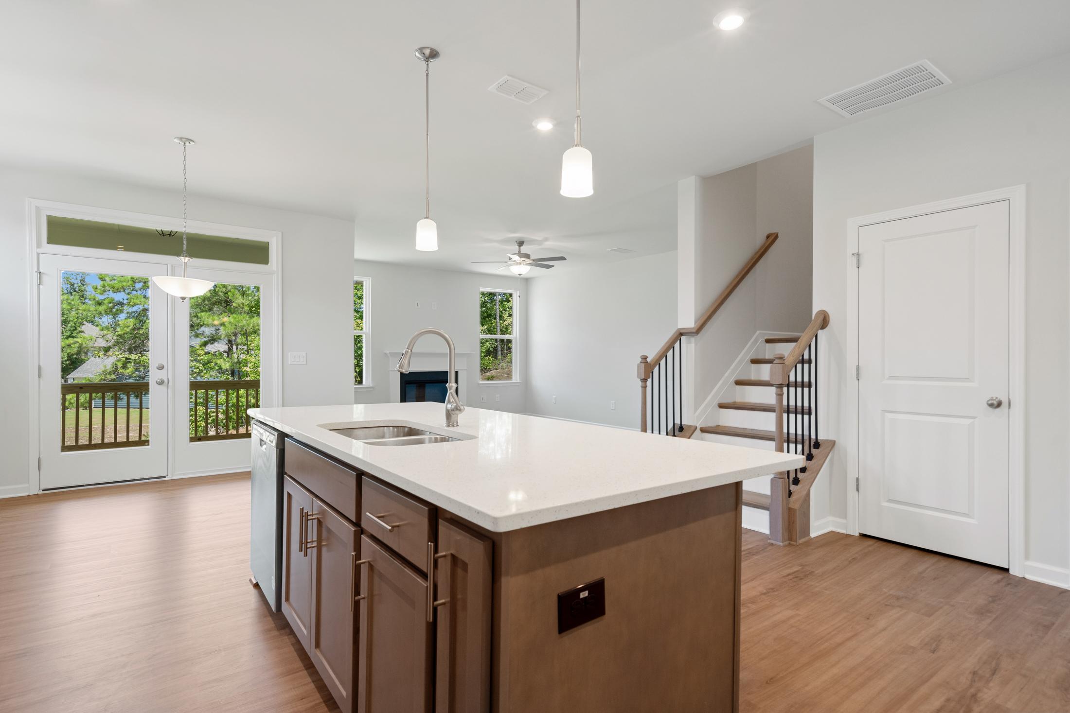 Open-concept kitchen living area in Mountainbrook Cartersville GA home with white quartz island, hardwood floors, French doors to deck, and fireplace