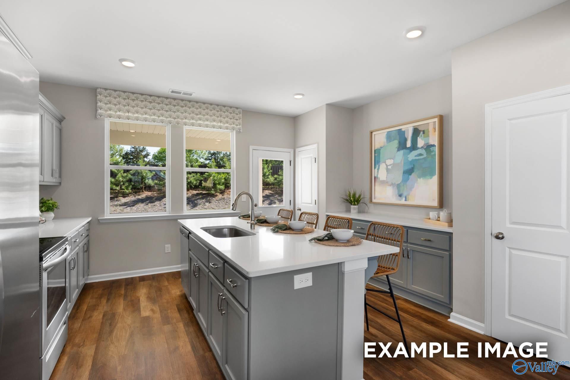 Modern kitchen featuring white cabinets, gray island with sink, stainless appliances in Davidson Homes The Stella, Madison, Alabama