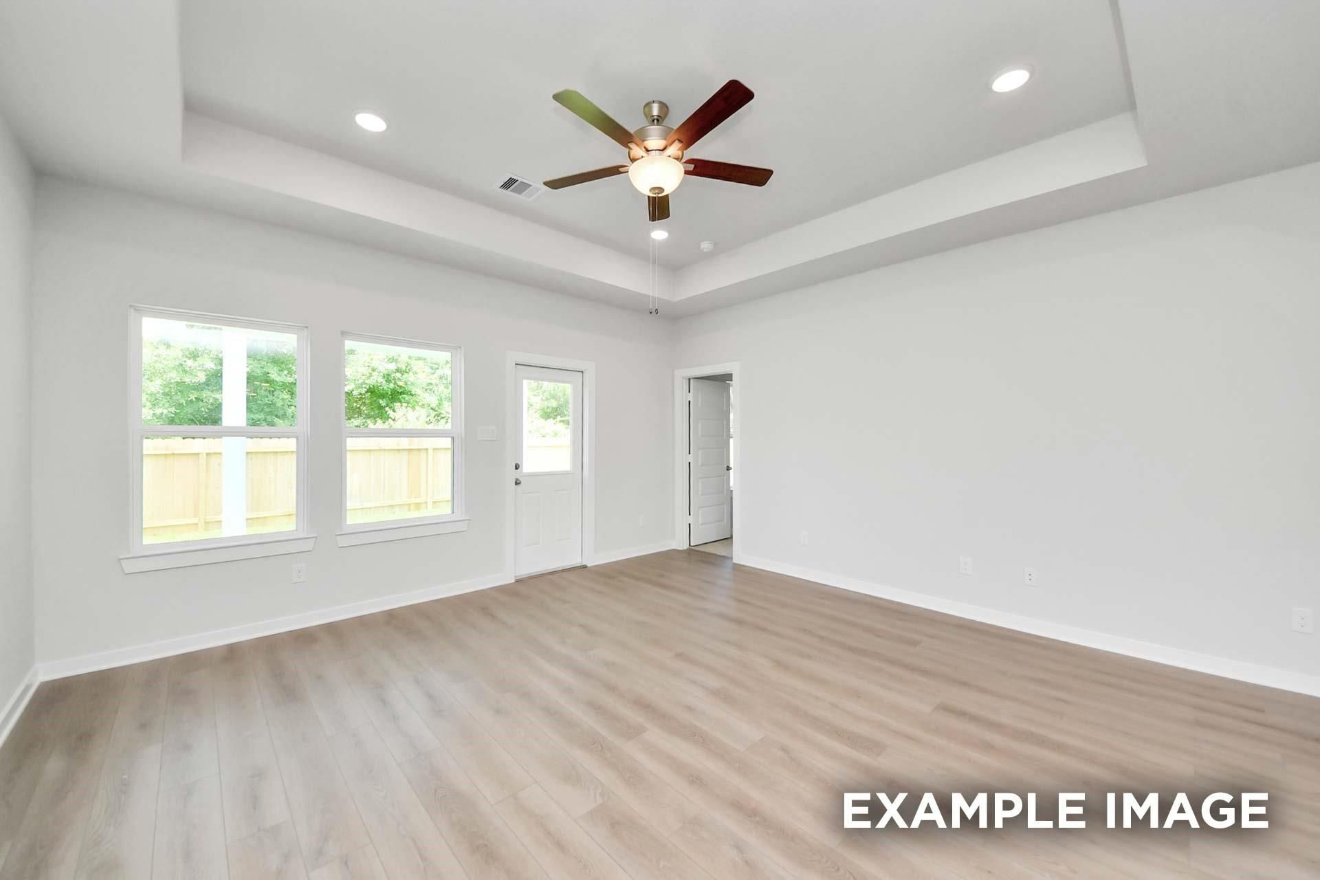 Bright spacious room with tray ceiling, ceiling fan, and wood-look flooring in Davidson Homes The Blanco E, Magnolia, Texas