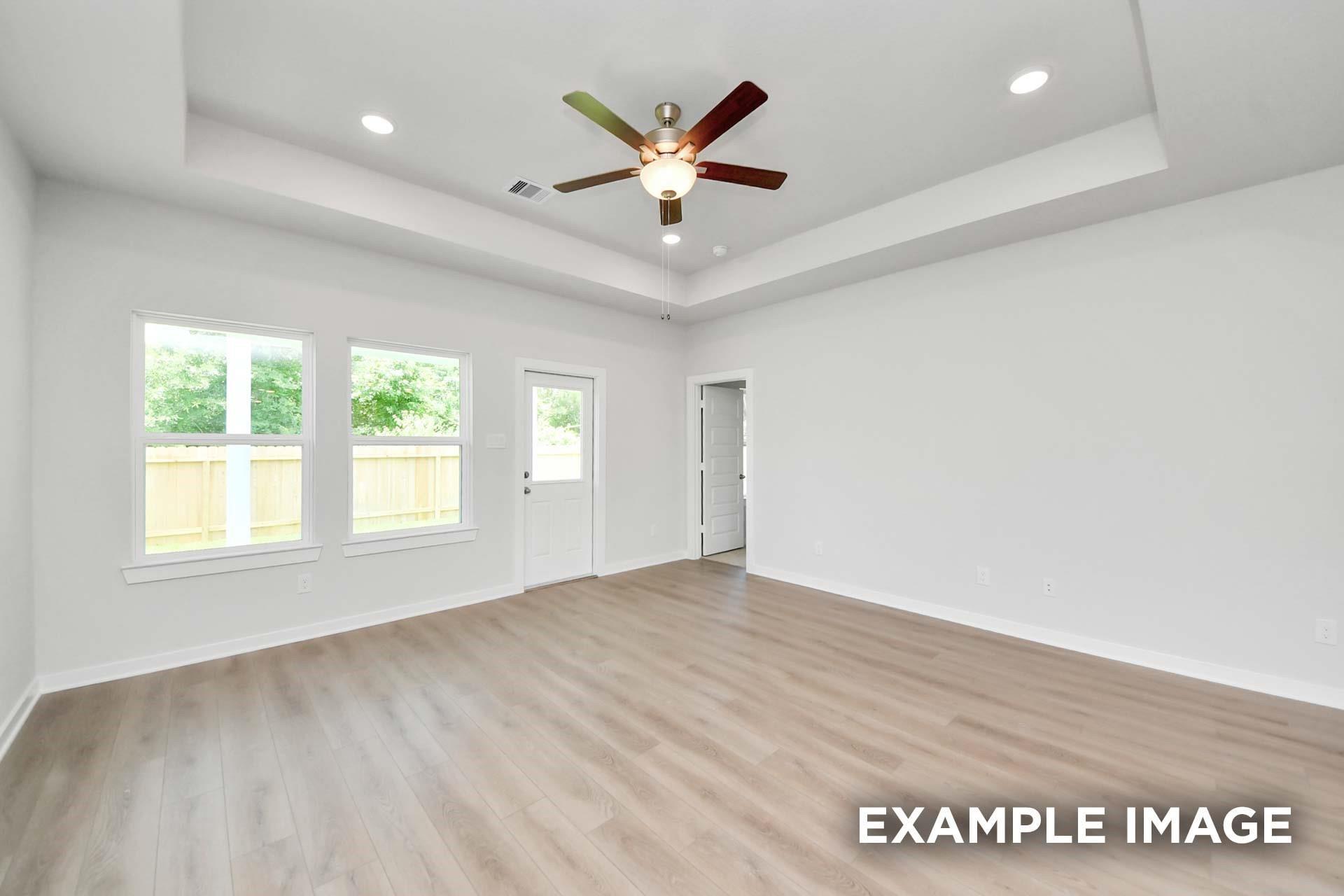 Bright spacious room with tray ceiling, ceiling fan, and wood-look flooring in Davidson Homes The Blanco E, Magnolia, Texas
