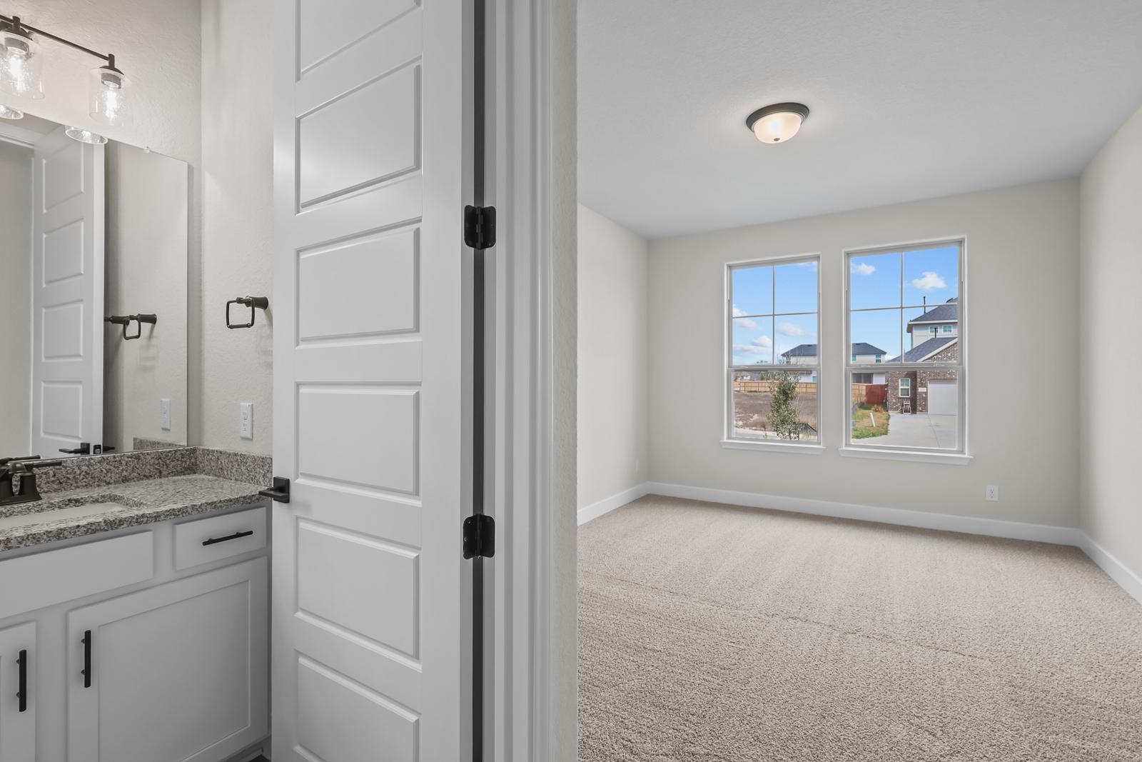 Spacious secondary bedroom and attached bathroom in The Belmont home featuring neutral finishes and large windows.