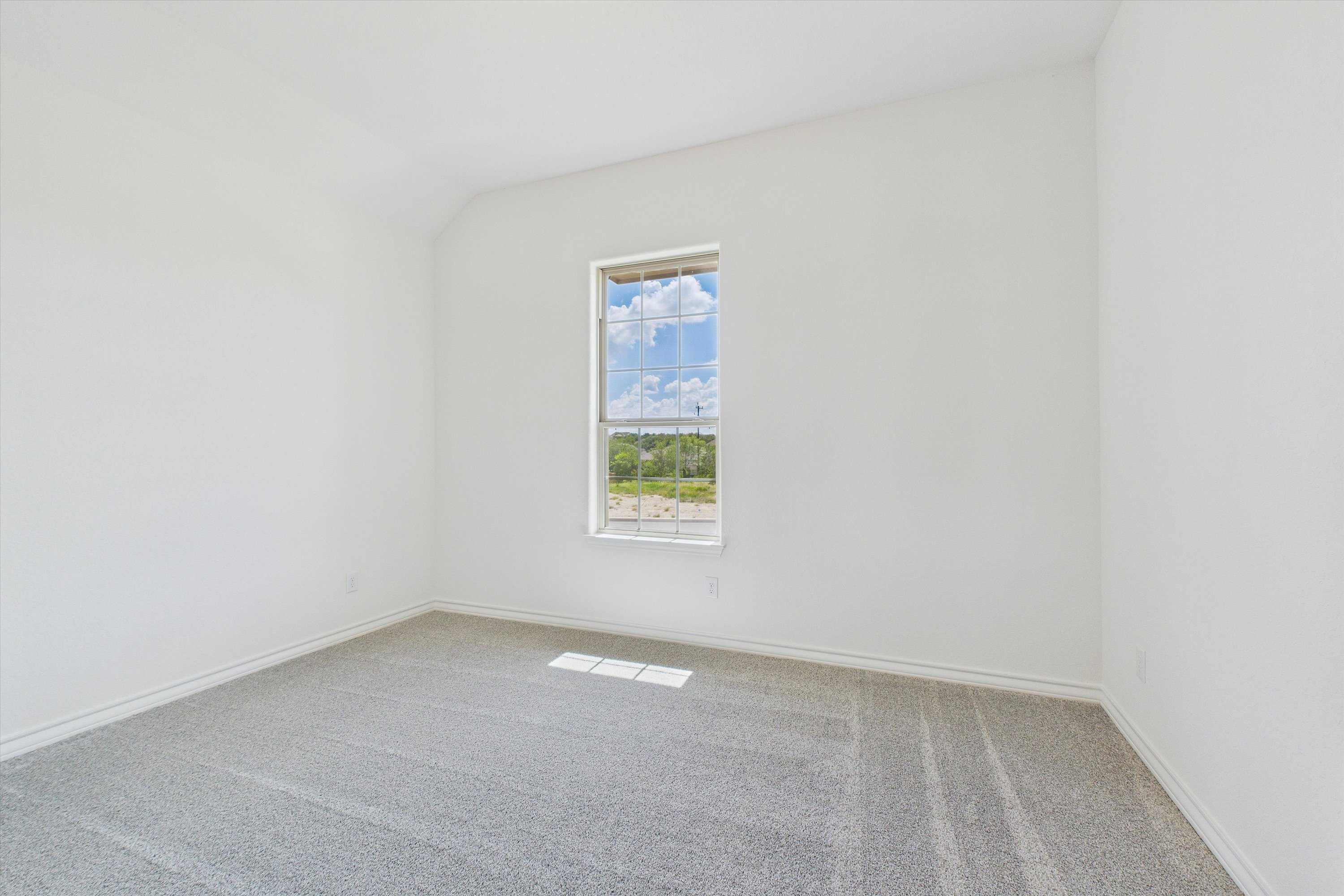 Bright secondary bedroom with white walls, carpet floor, and window view of green fields in Davidson Homes Summerlin C, Castroville, Texas