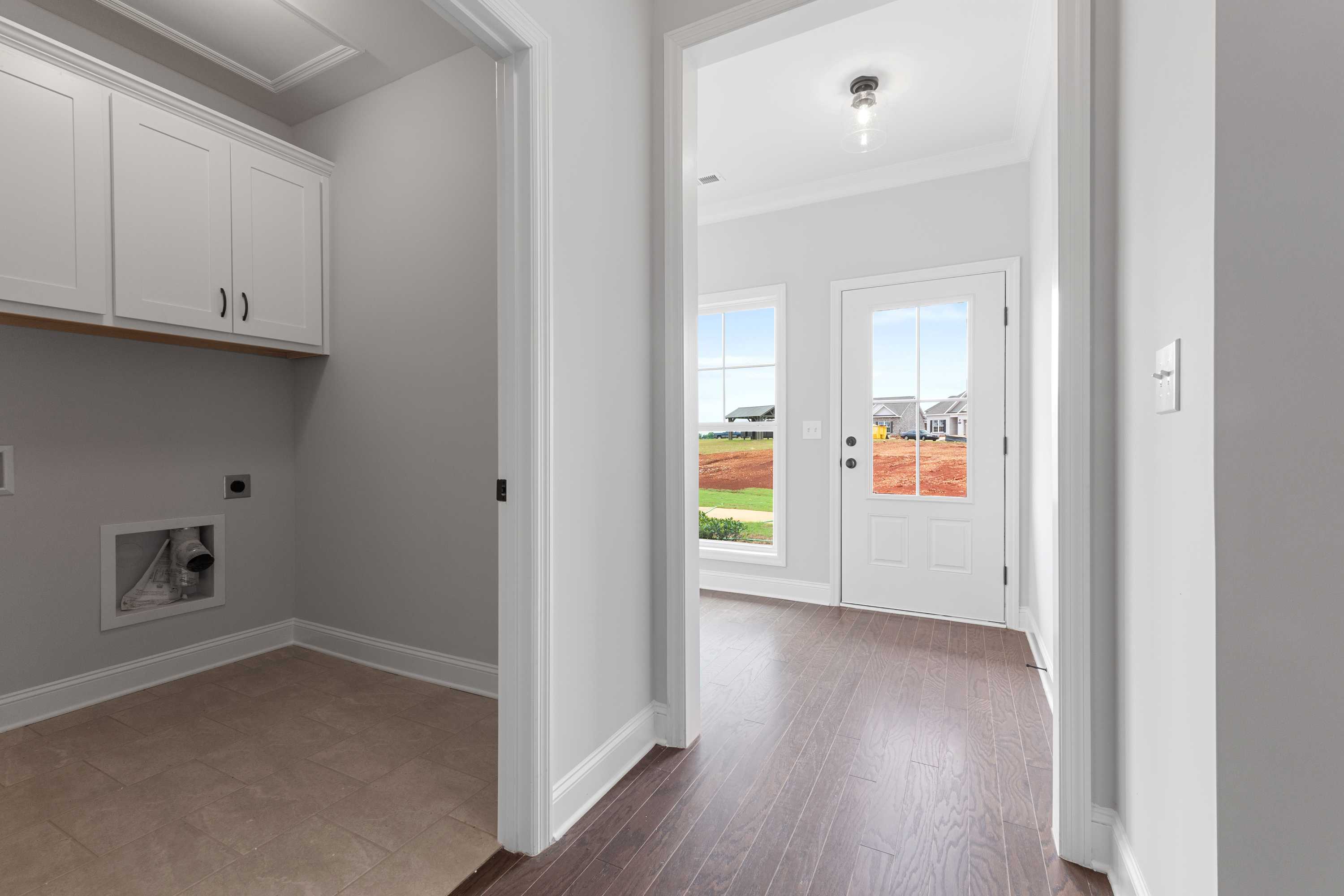 Spacious laundry room with white cabinets and washer hookups adjacent to hardwood hallway at The Villas at Barnett's Crossing in Madison, Alabama