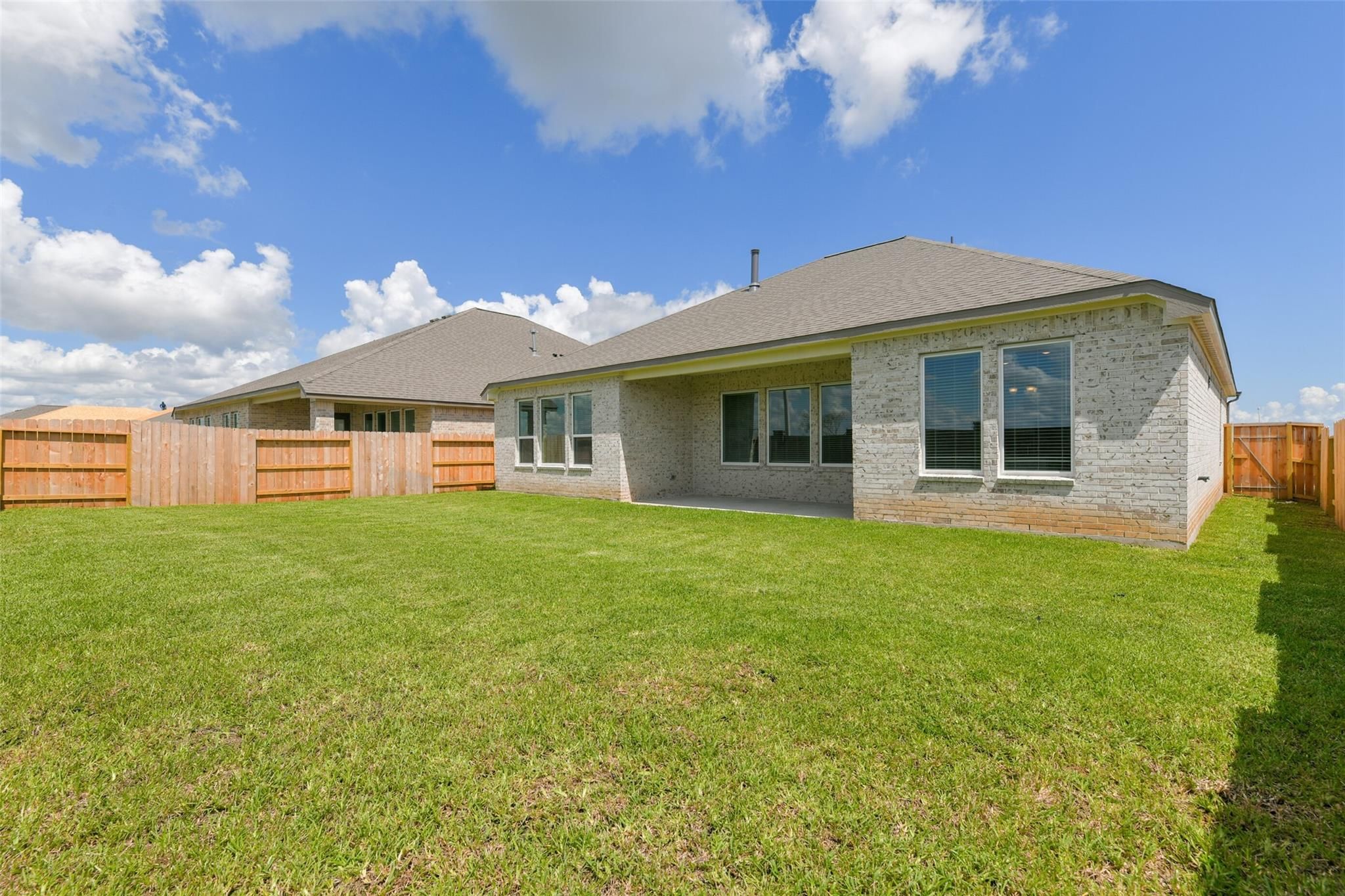 Covered back patio with large sliding doors and windows on brick home, lush green yard, wooden fence in Lago Mar, Texas City