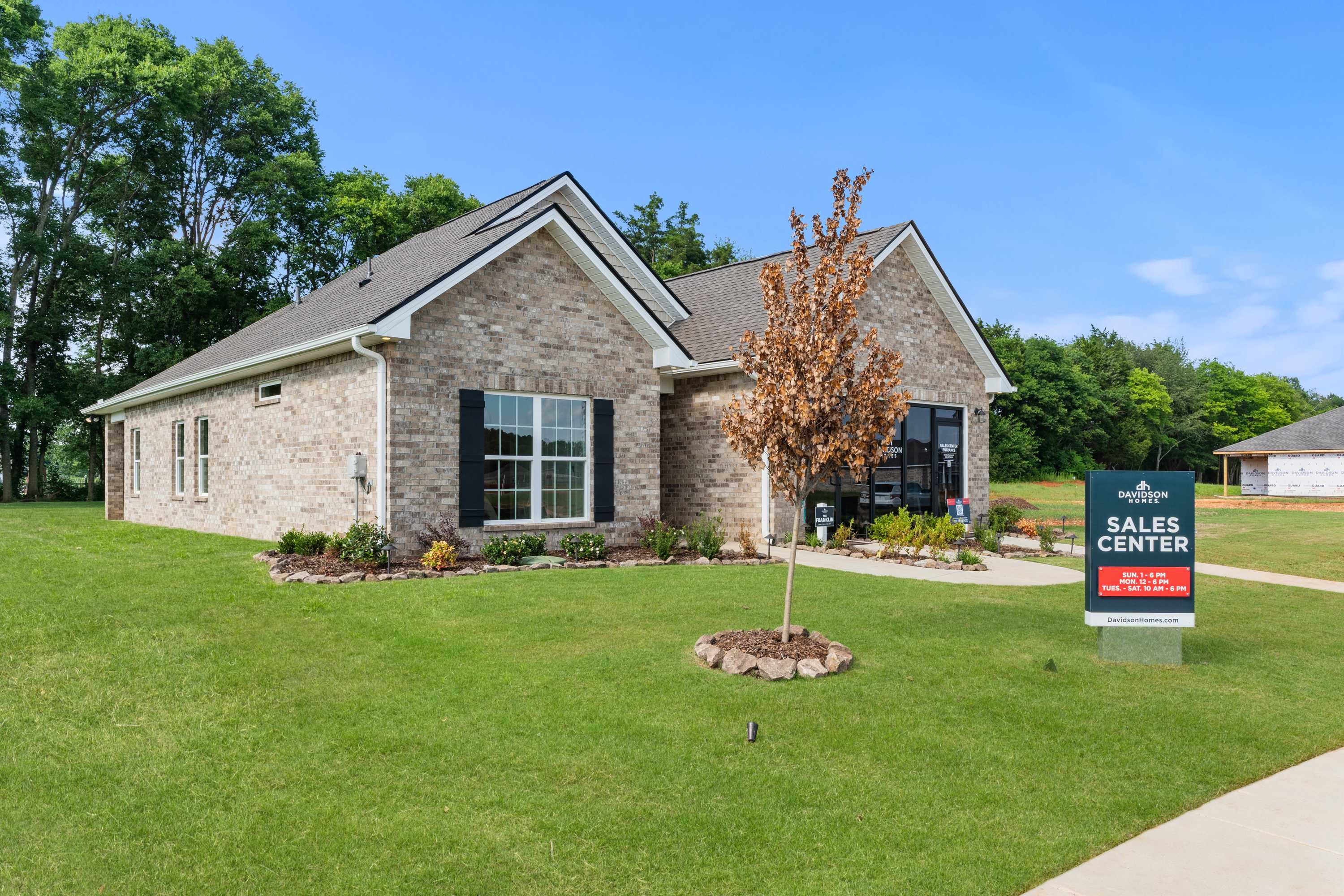 Brick home exterior at Lynn Meadows in Meridianville Alabama with gabled roof, large windows, landscaped yard and sales center sign