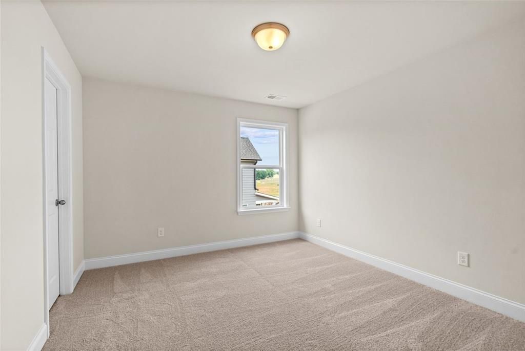 Bright secondary bedroom with beige walls, neutral carpet, and large window in Davidson Homes The Hickory B at Wehunt Meadows, Hoschton