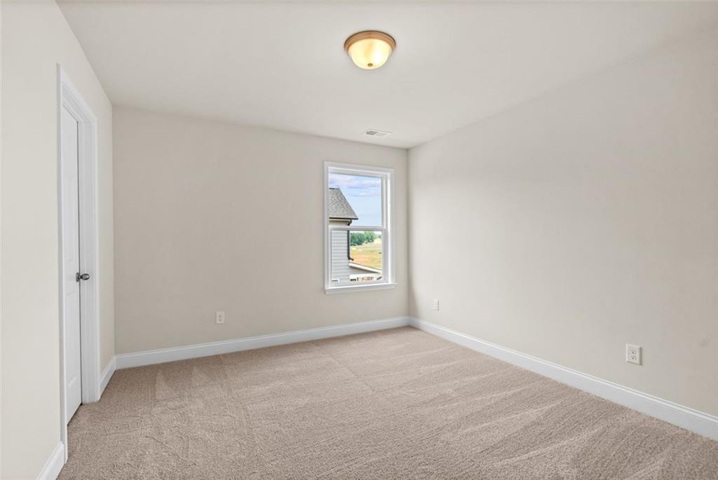 Bright secondary bedroom with beige walls, neutral carpet, and large window in Davidson Homes The Hickory B at Wehunt Meadows, Hoschton