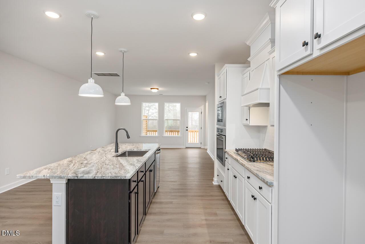 Open-concept kitchen with white shaker cabinets, swirled granite island, stainless appliances, and deck view in Davidson Homes The Mitchell, Knightdale, NC