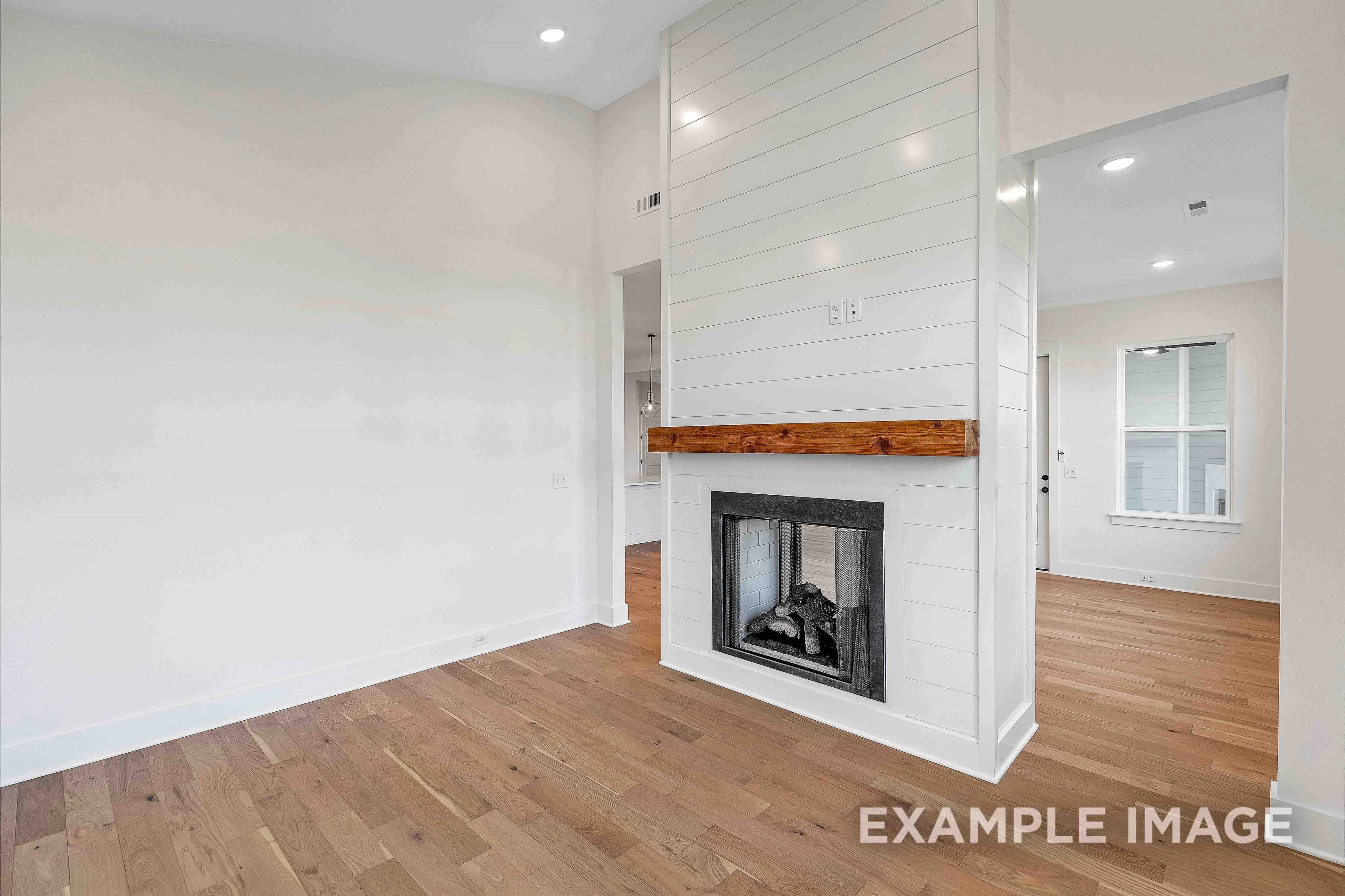 Spacious living room in The Albany A featuring white shiplap fireplace with wooden mantel, hardwood floors, open layout