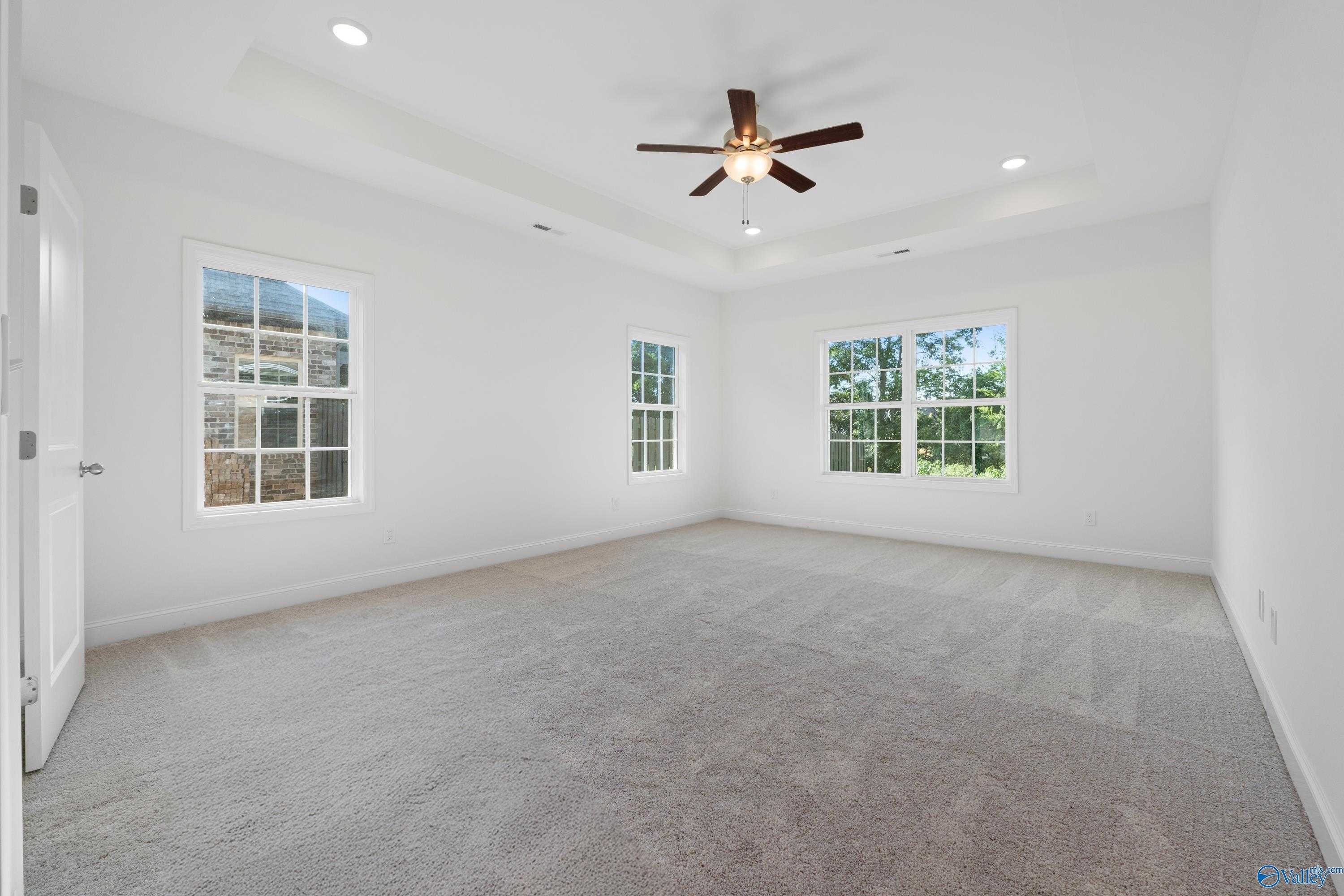 Bright bedroom with large windows, ceiling fan, recessed lights, and plush carpet in Davidson Homes The Oxford, Harvest, Alabama