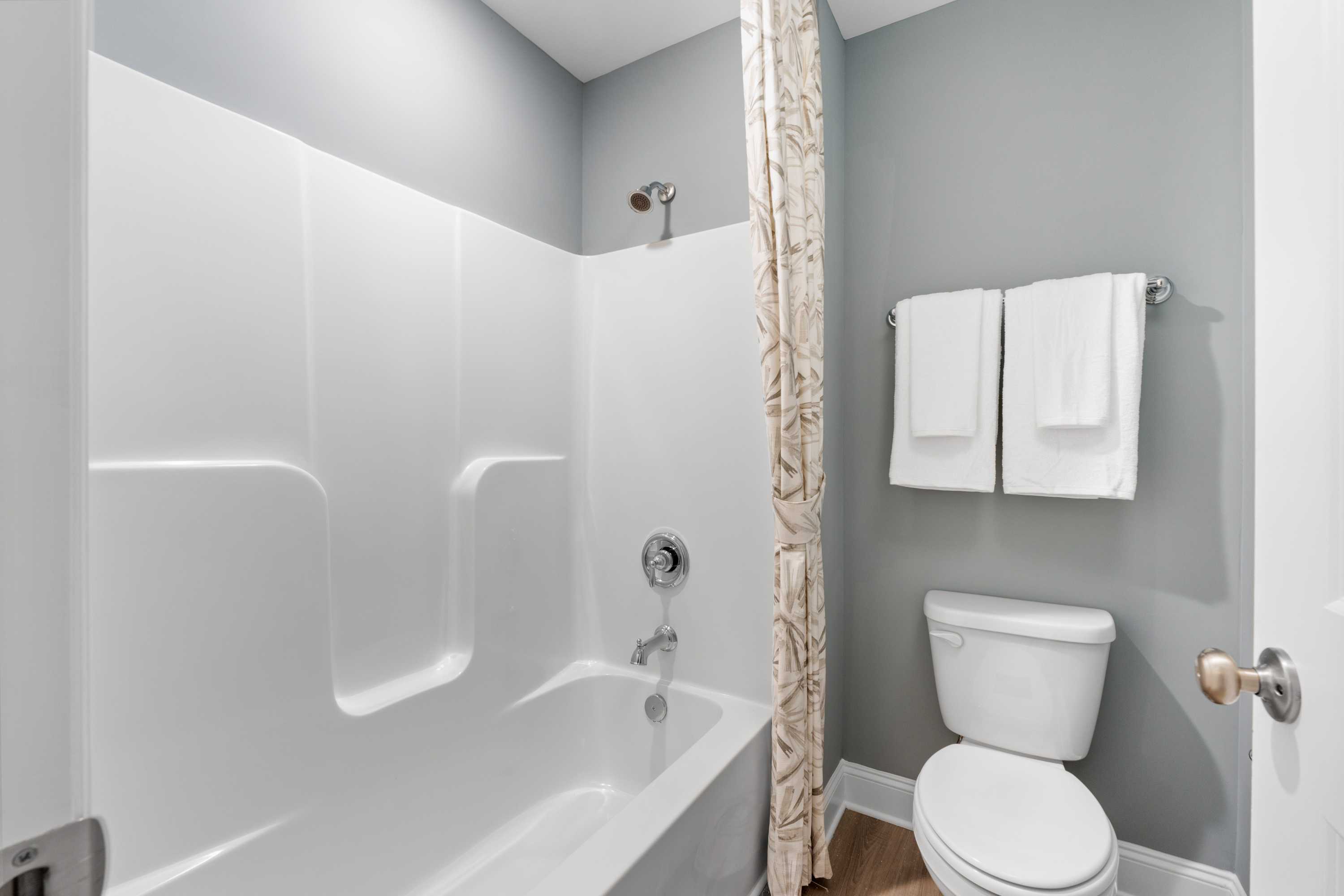Spacious bathroom with white tub-shower combo, gray walls, patterned curtain, white toilet, and towels in Pavilion Huntsville AL home by Davidson Homes
