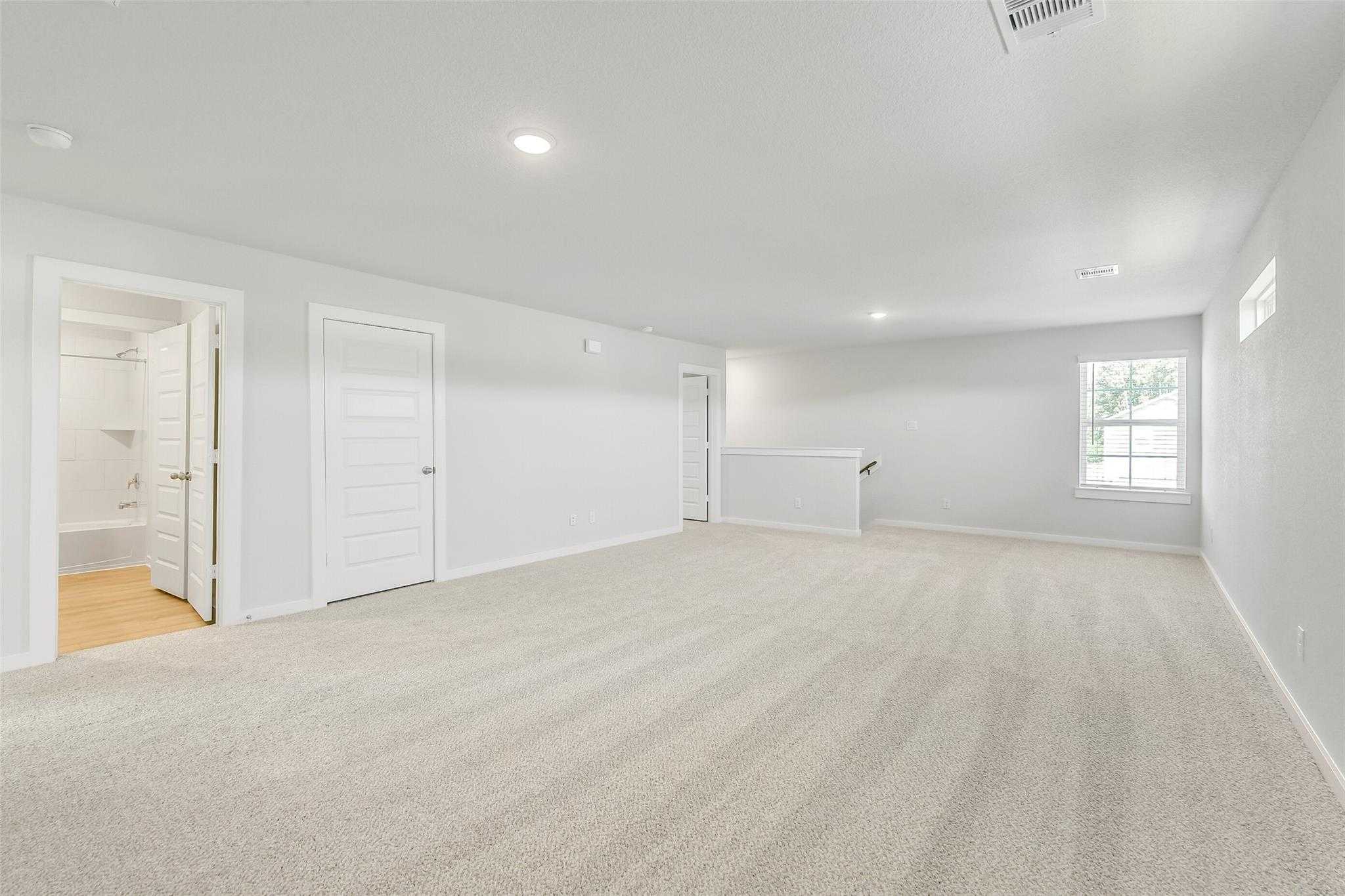 Spacious upstairs loft with beige carpet, white walls, bathroom doors, and large window in Davidson Homes The San Marcos E, Cleveland, Texas