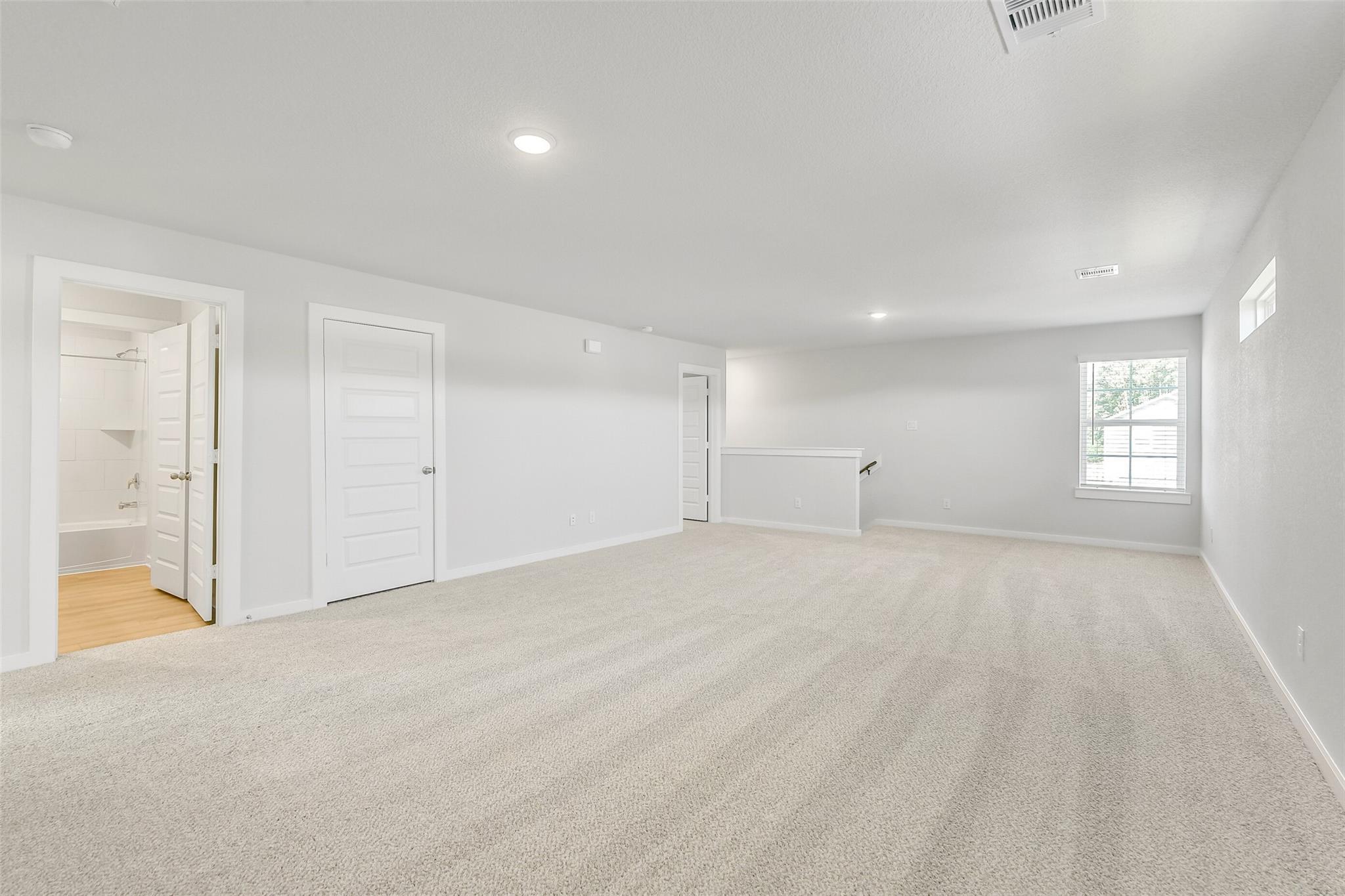 Spacious upstairs loft with beige carpet, white walls, bathroom doors, and large window in Davidson Homes The San Marcos E, Cleveland, Texas