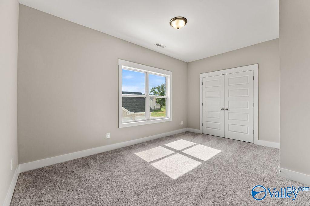 Bright bedroom with large window, double closet doors, and neutral walls in Evermore Homes The Oxford, Owens Cross Roads, Alabama