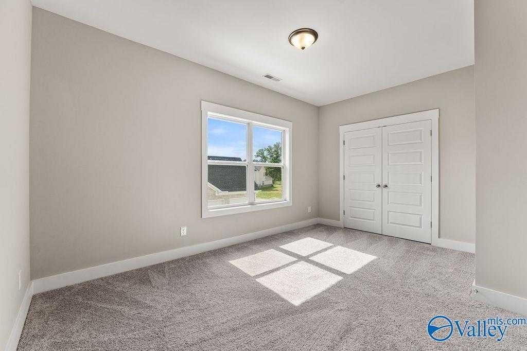 Bright bedroom with large window, double closet doors, and neutral walls in Evermore Homes The Oxford, Owens Cross Roads, Alabama