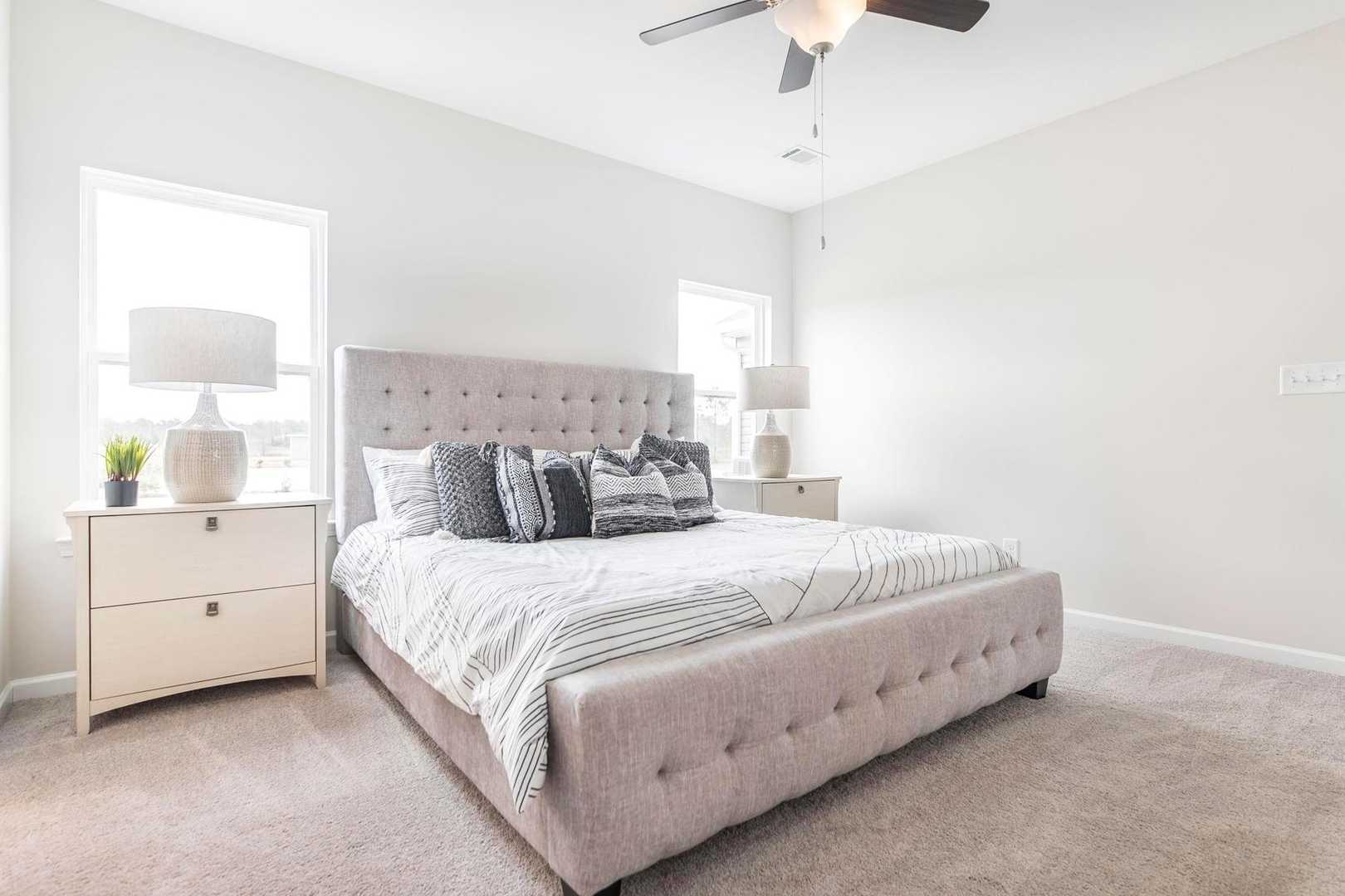 Spacious primary bedroom at Cape Reserve at Donahue Ridge in Auburn Alabama with tufted upholstered bed, ceiling fan and neutral decor